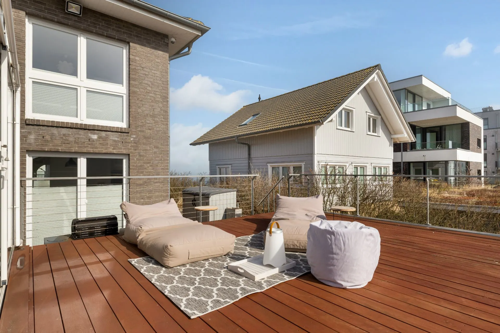 Große Terrasse mit Sitzsäcken, Teppich und Tisch, umgeben von Wohnhäusern.
