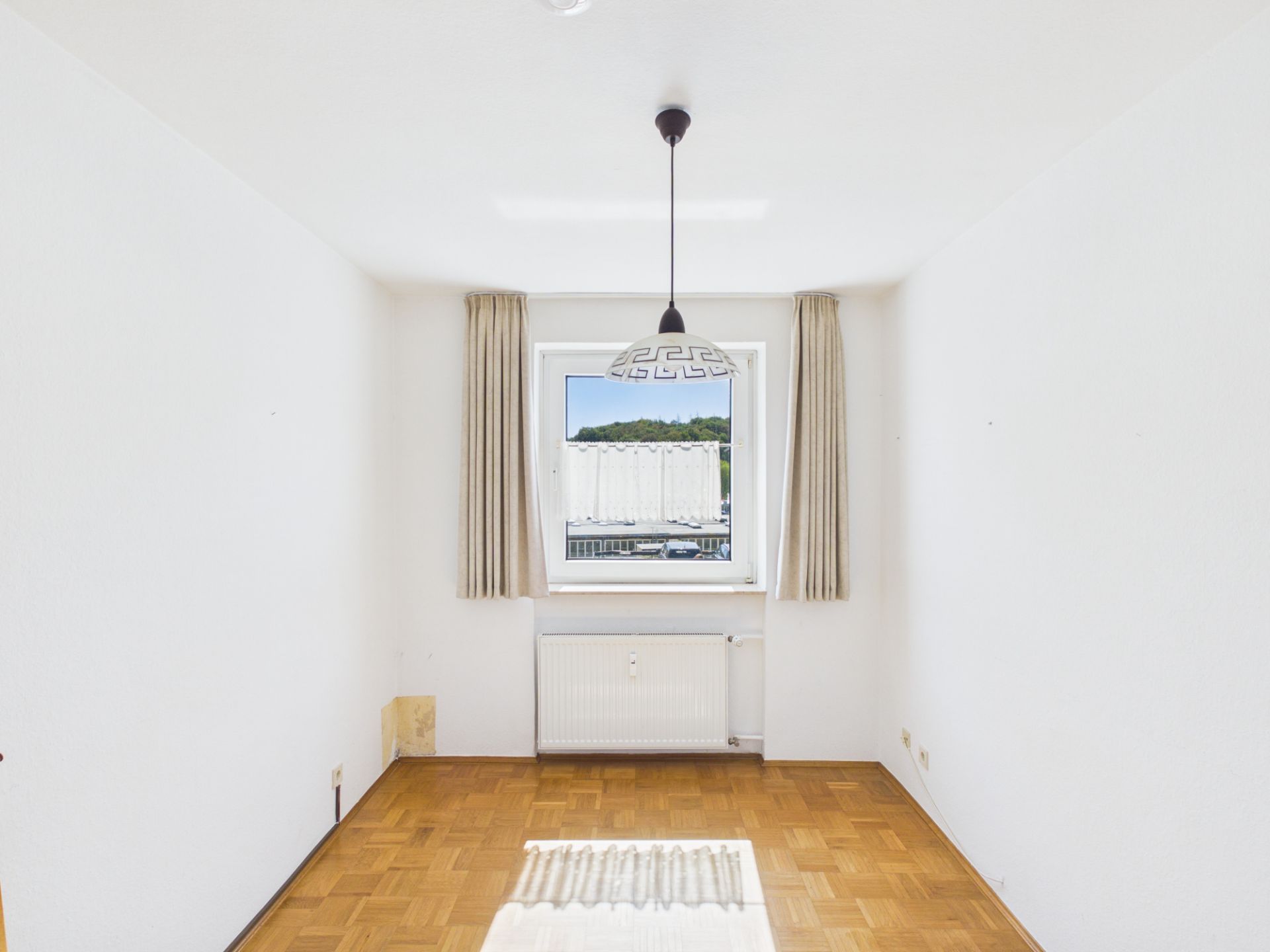 Leerer Raum mit Parkettboden, Fenster, Vorhängen und Deckenlampe.
