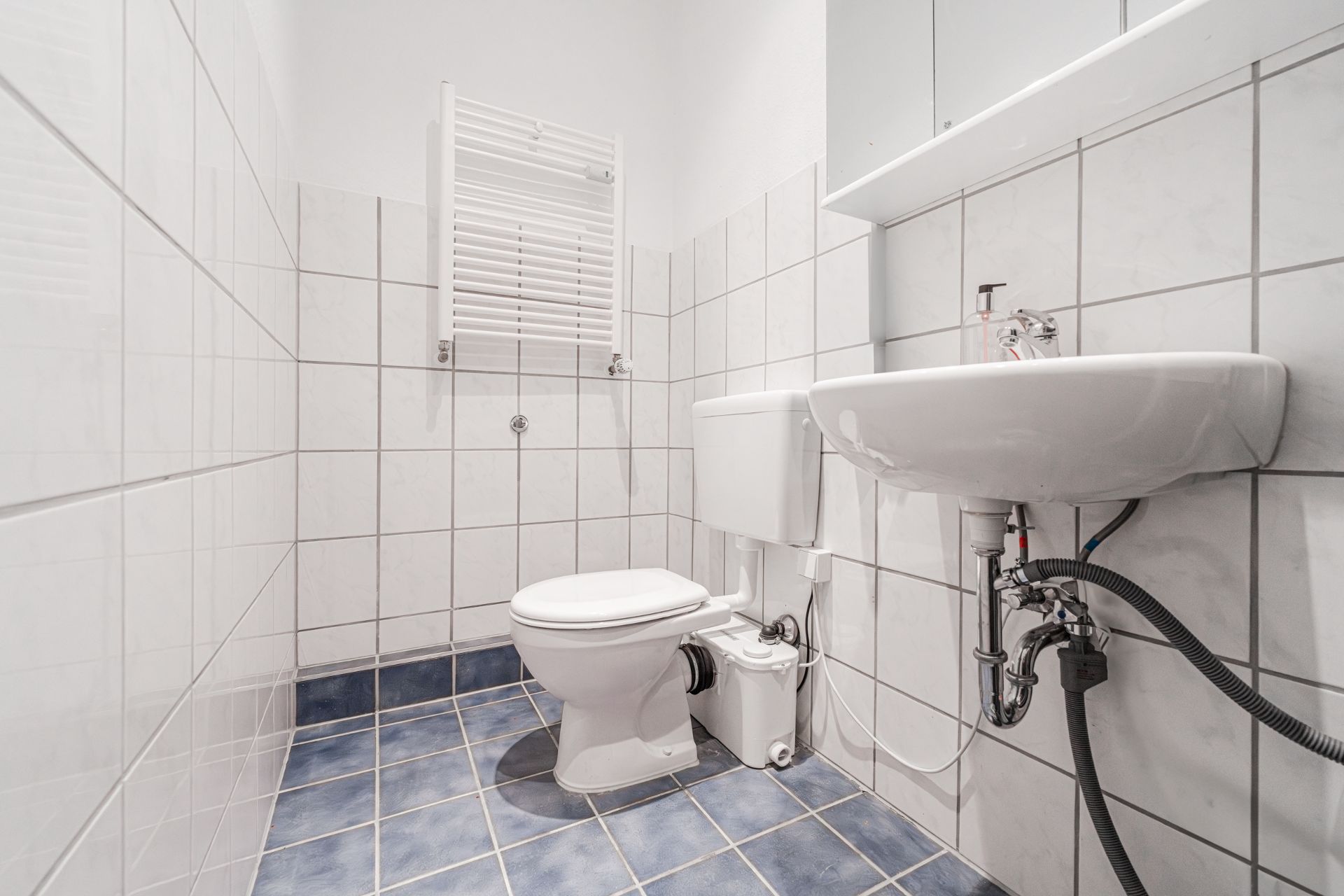 Kleines Badezimmer mit weißer Toilette und Waschbecken, gefliest mit blauem Boden.