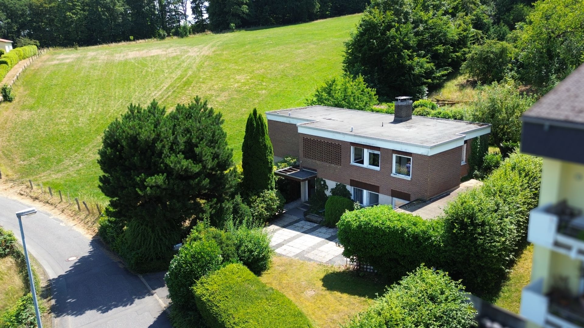 Zweistöckiges Wohnhaus mit Flachdach und großem Garten, umgeben von Bäumen und Büschen.