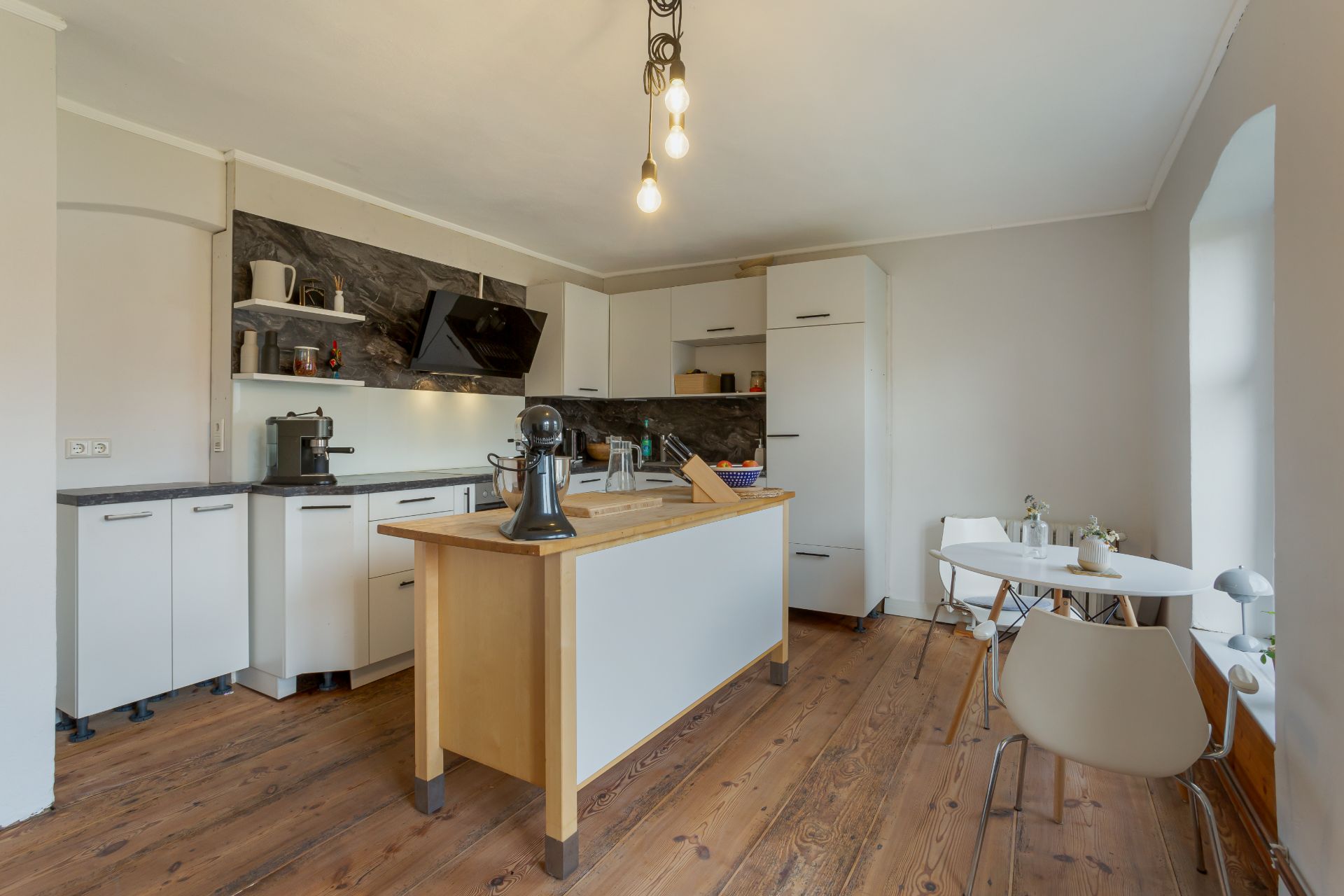 Moderne Küche mit Kücheninsel, Holzboden und kleinem Esstisch mit zwei Stühlen.