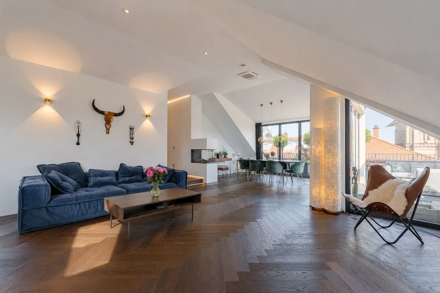 Modernes Wohnzimmer mit blauem Sofa, Couchtisch, Esstisch und großen Fenstern.