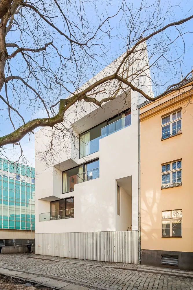 Modernes weißes Wohnhaus mit großen Fenstern und Balkonen, daneben ältere Gebäude.
