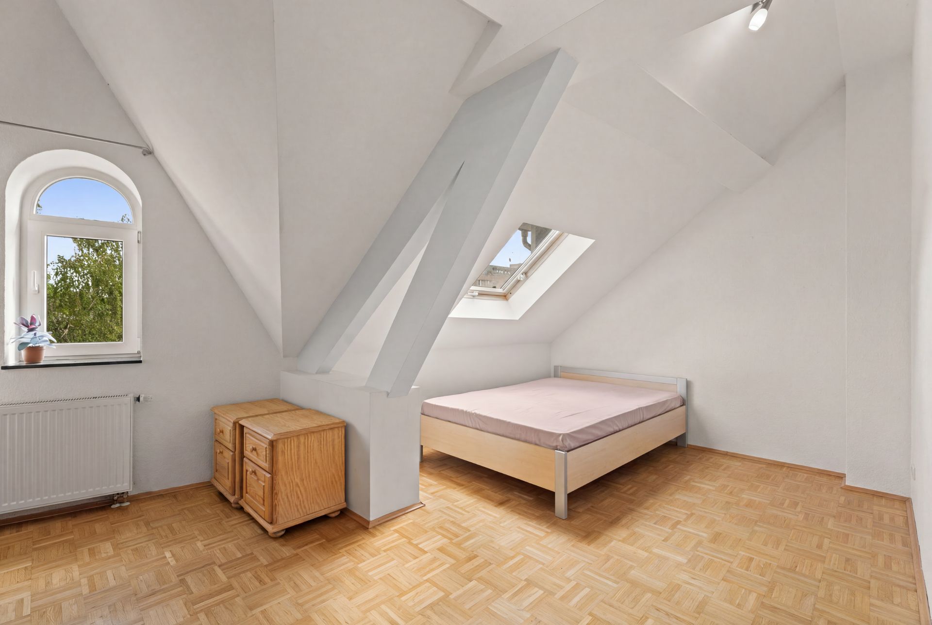 Helles Schlafzimmer mit Dachschräge, Bett, Nachttisch und zwei Fenstern.