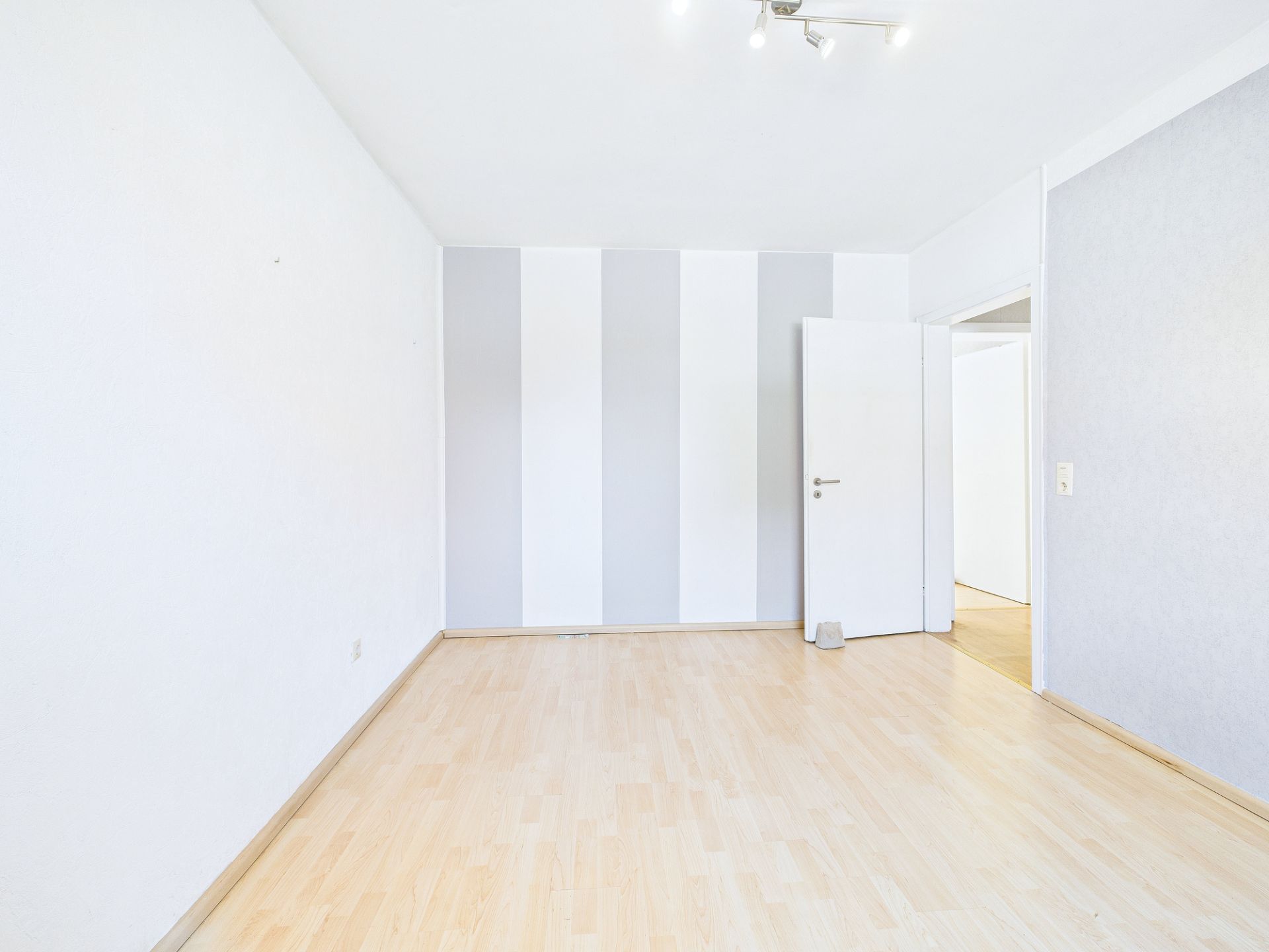 Helles, leeres Zimmer mit Holzfußboden und gestreifter Wand.