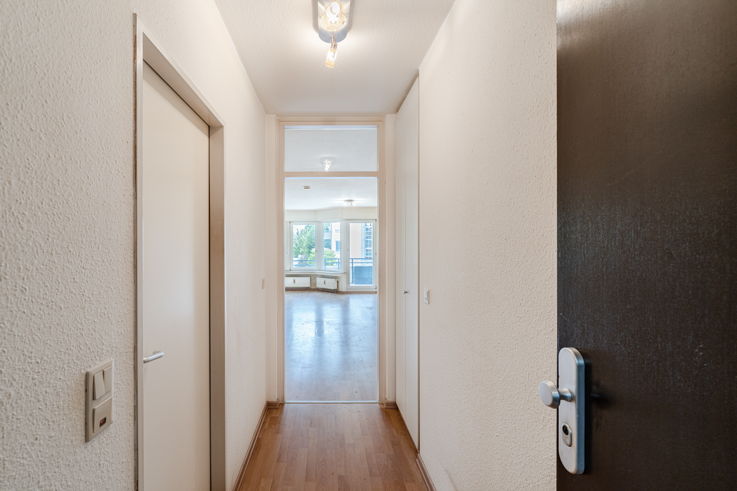 Heller Flur mit Holzboden und Türen, Blick in ein großes Wohnzimmer mit Fenstern.
