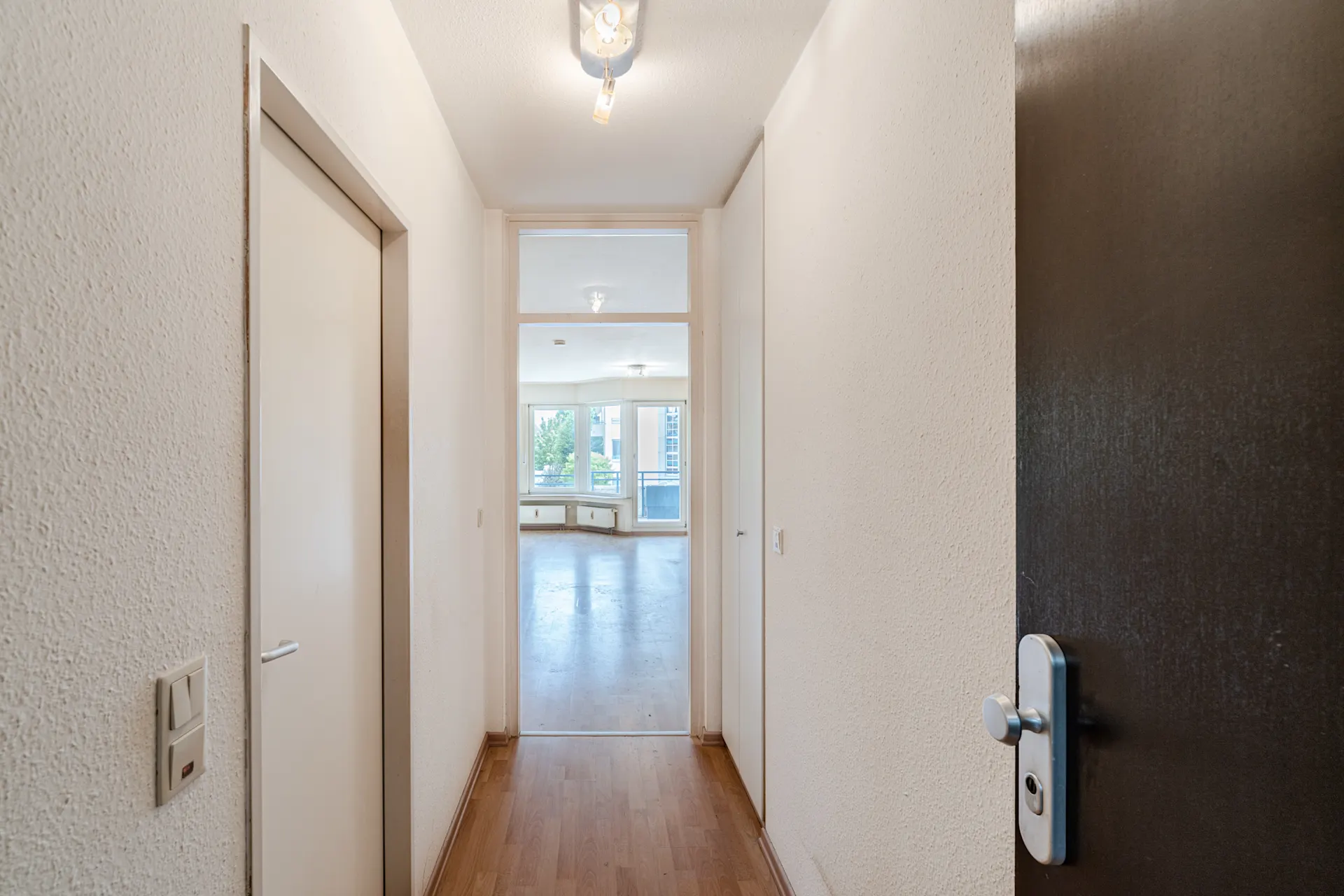 Heller Flur mit Holzboden und Türen, Blick in ein großes Wohnzimmer mit Fenstern.