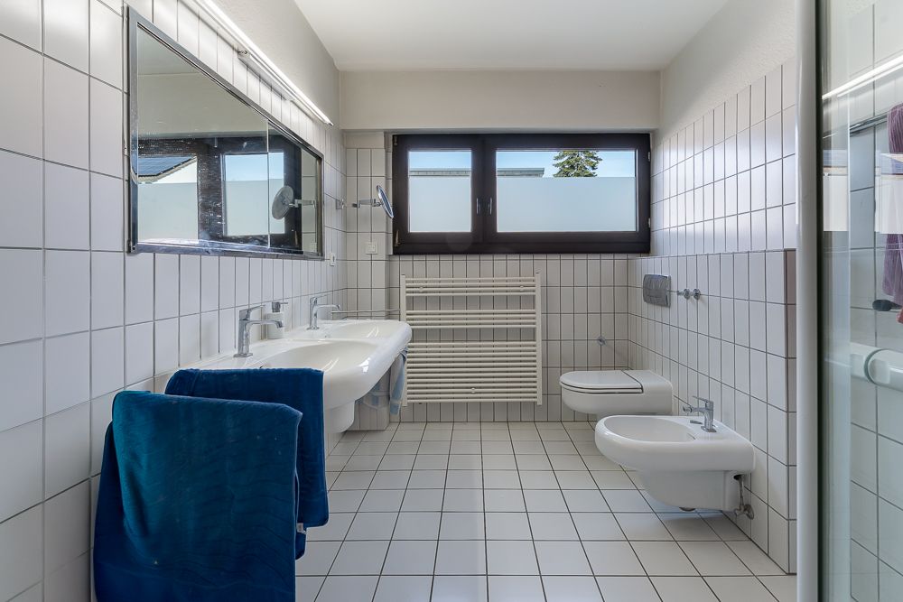 Modernes Badezimmer mit zwei Waschbecken, Bidet, WC, großem Fenster und Handtuchheizkörper.