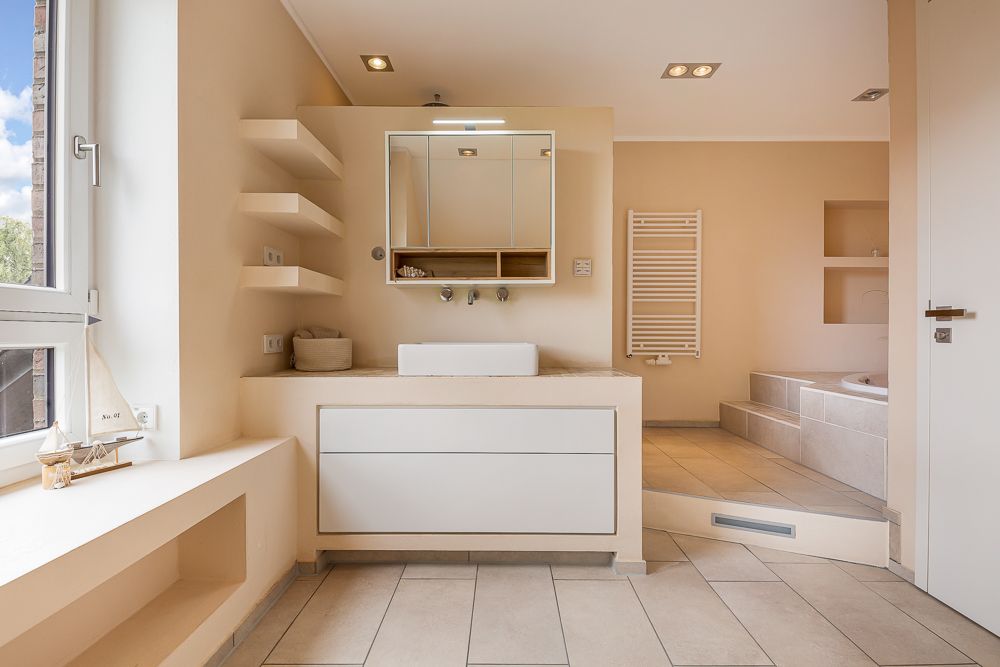 Modernes Badezimmer mit Waschbecken, Spiegel, Regal, Fenster und Badewanne auf erhöhter Fläche.
