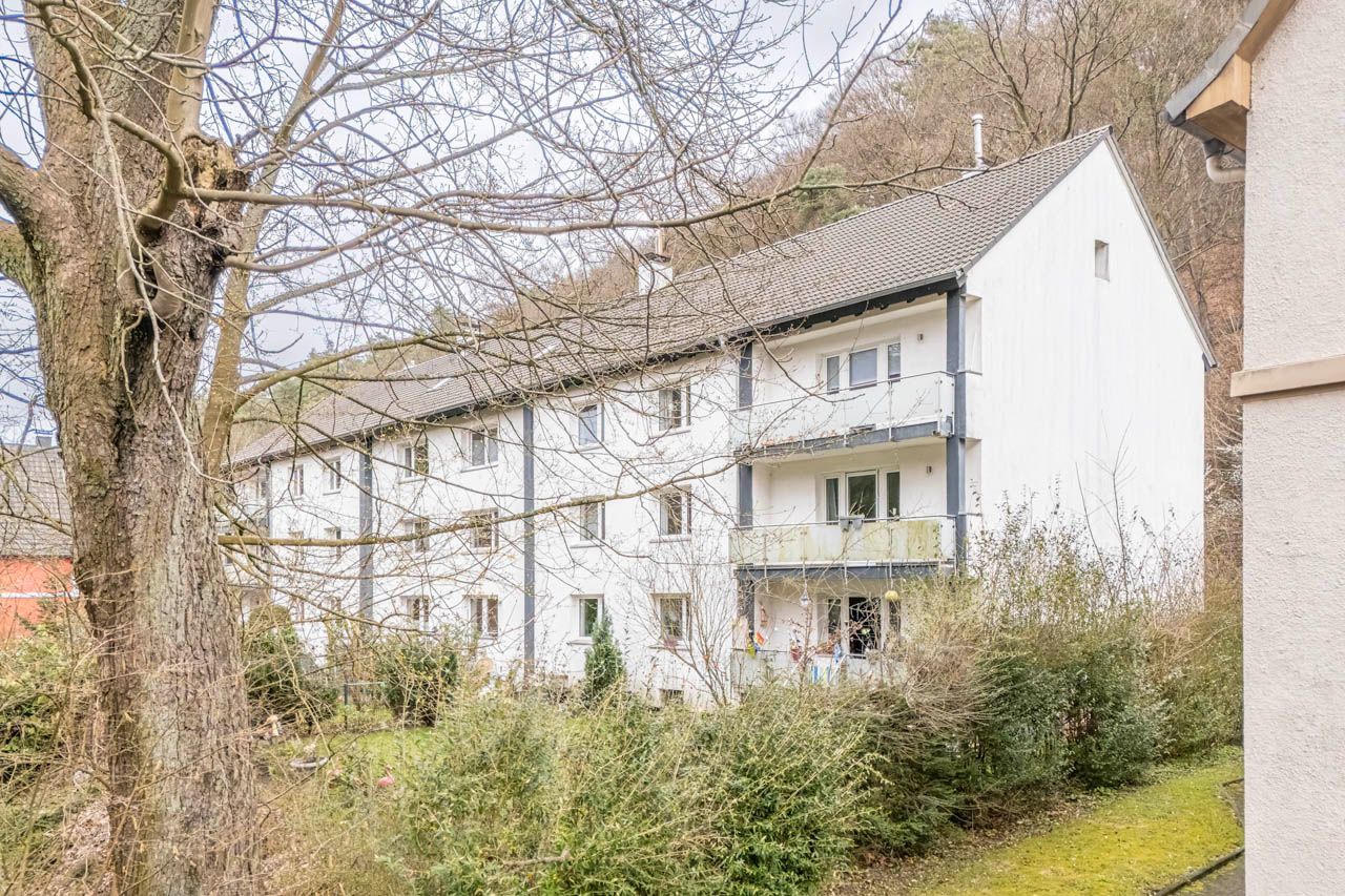 Mehrfamilienhaus mit weißer Fassade, mehreren Balkonen und umliegenden Bäumen.