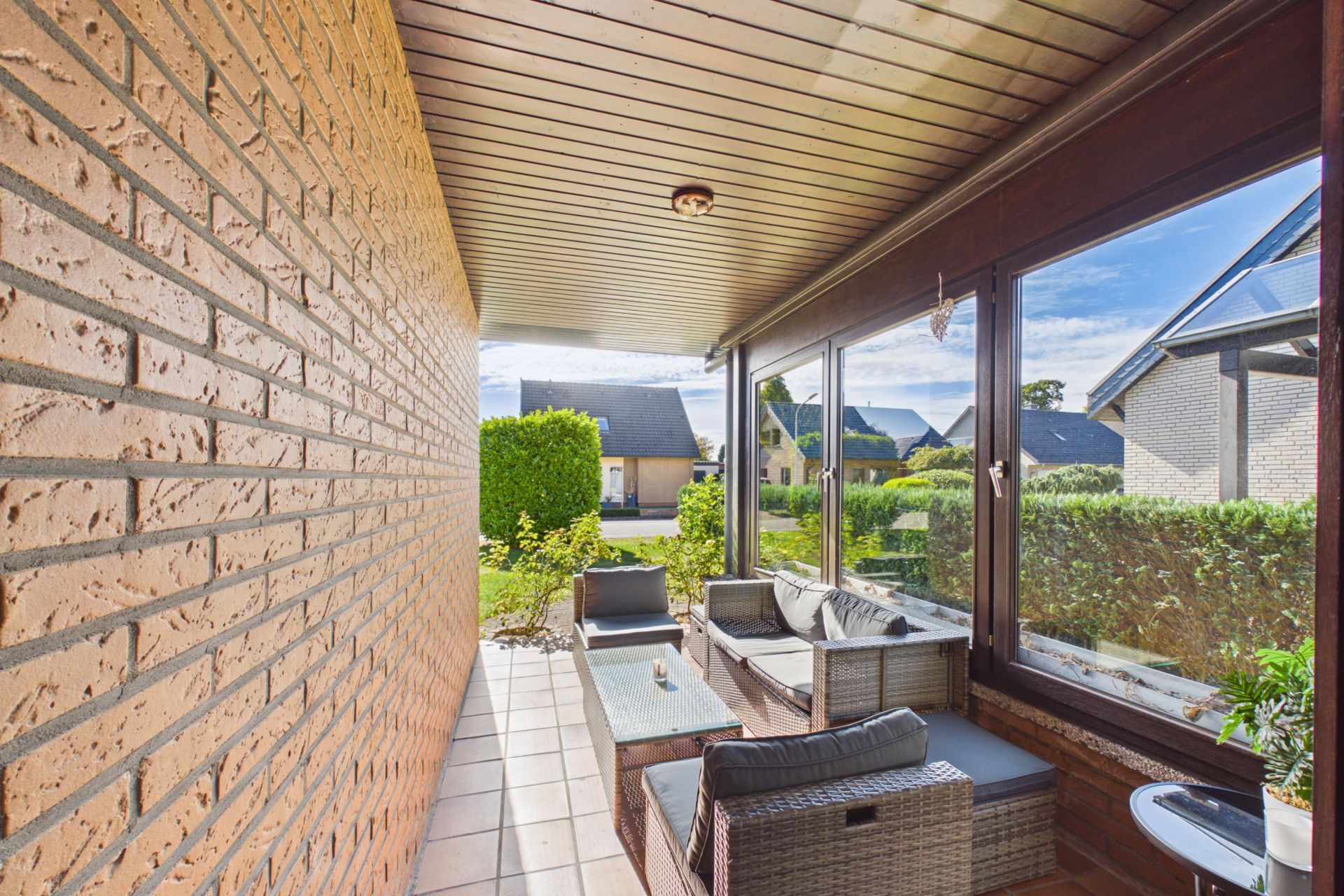Überdachte Terrasse mit Sitzmöbeln, Glastüren und Blick auf Nachbarhäuser und Garten.