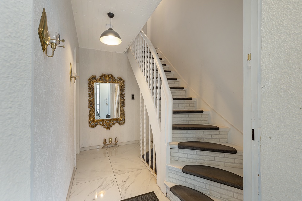 Heller Flur mit Marmorboden, weißer Treppe und großem goldenen Spiegel an der Wand.