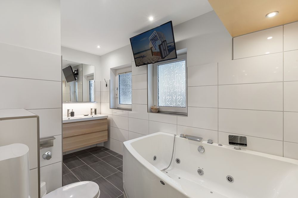 Modernes Badezimmer mit großer Badewanne, Waschbecken, Spiegel und Wandfernseher.
