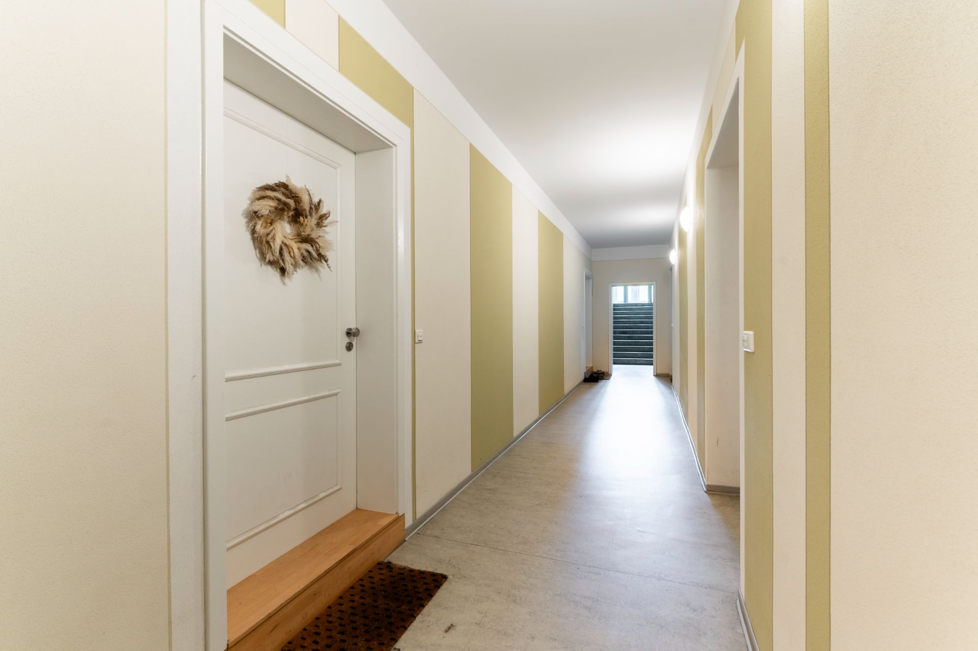 Heller Flur mit weißen und beigen Wänden, einer Wohnungstür und Dekokranz.
