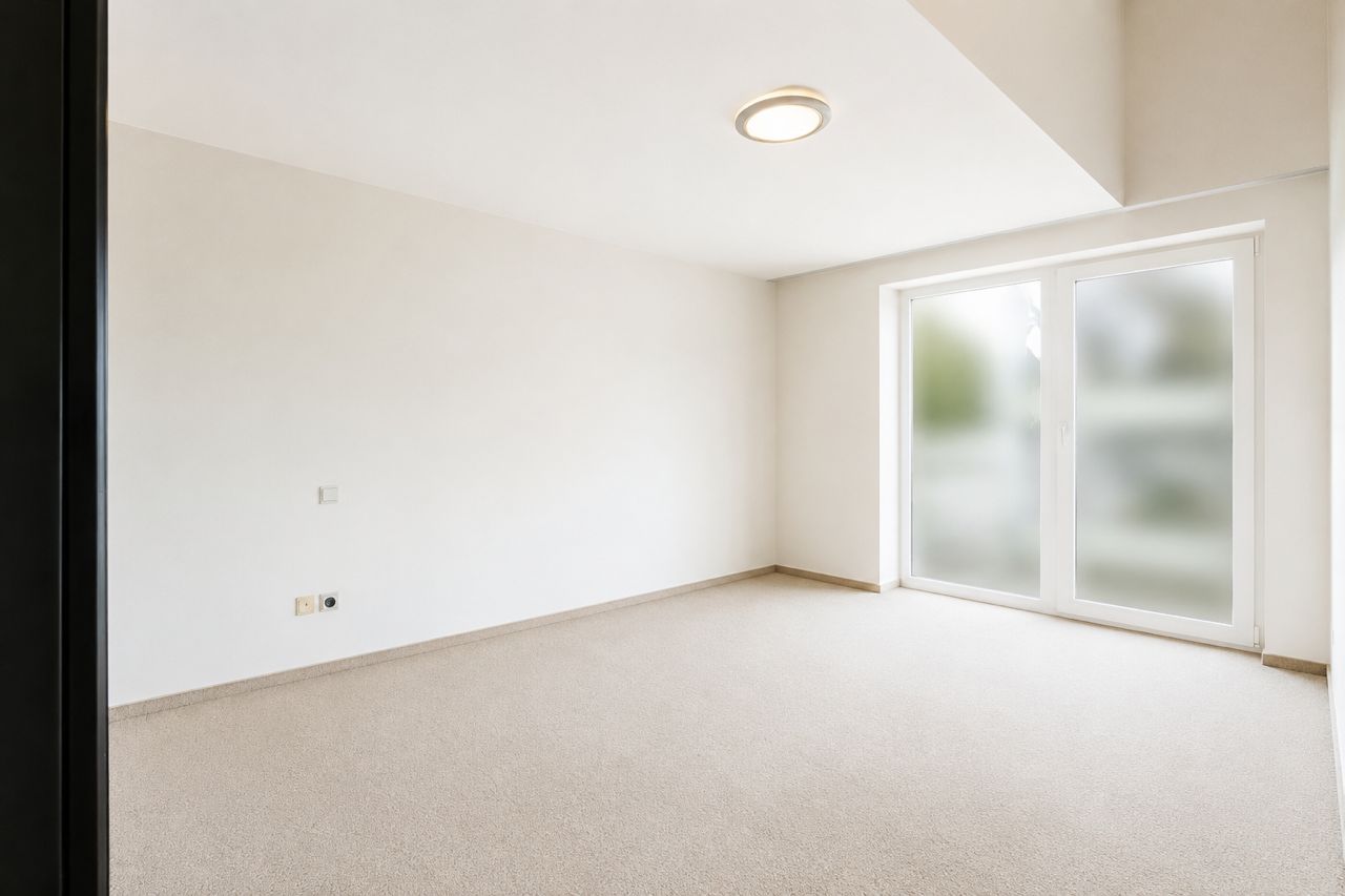 Heller, leerer Raum mit Teppichboden und großer Fenstertür.