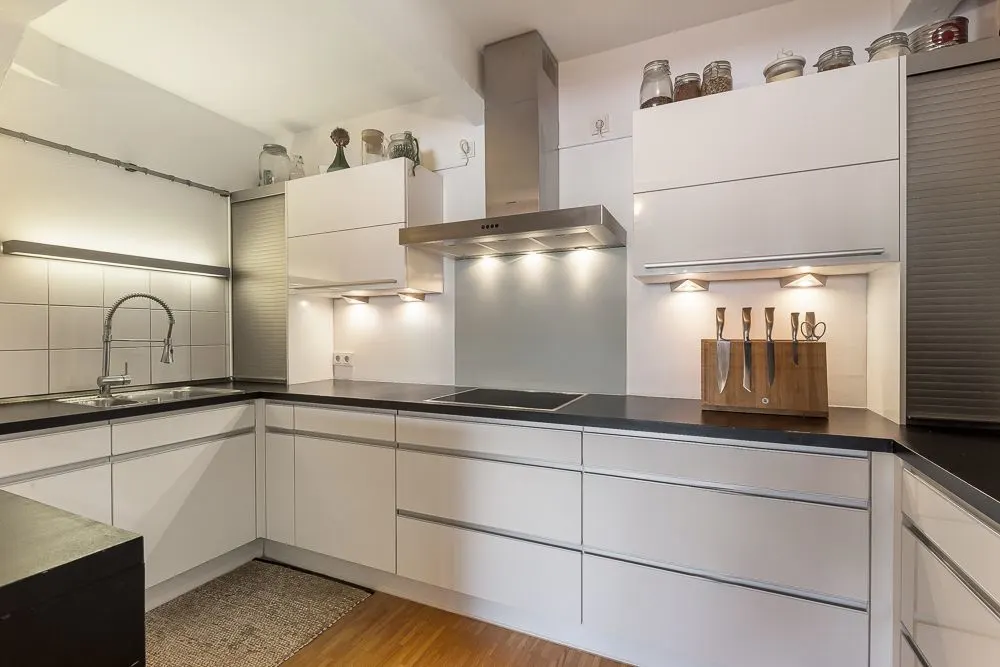 Moderne weiße Einbauküche mit Kochfeld, Dunstabzugshaube und Messerblock auf der Arbeitsplatte.
