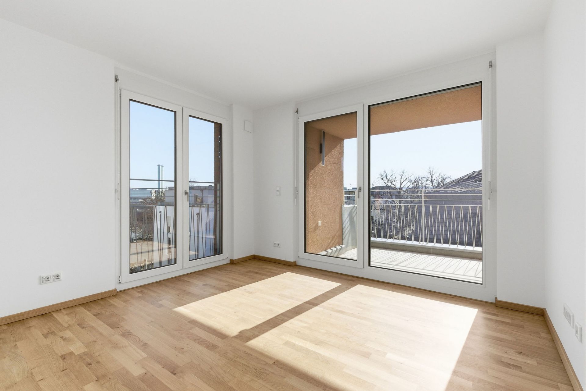 Helles Zimmer mit Parkettboden und großen Fenstern zu einem Balkon.