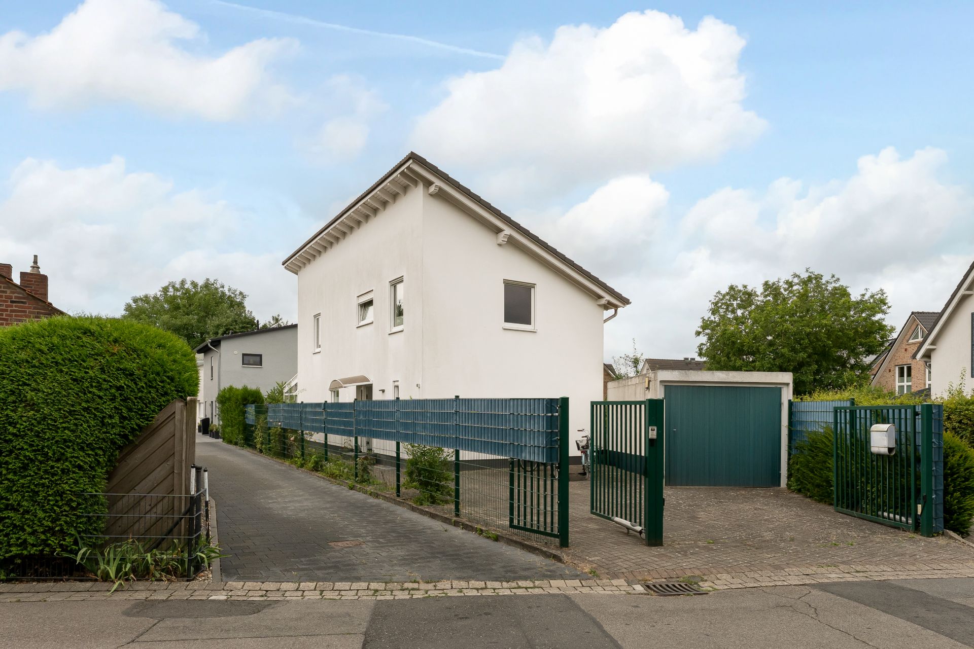 Modernes, weißes Wohnhaus mit grünem Zaun und Einfahrt, Tor ist geöffnet.