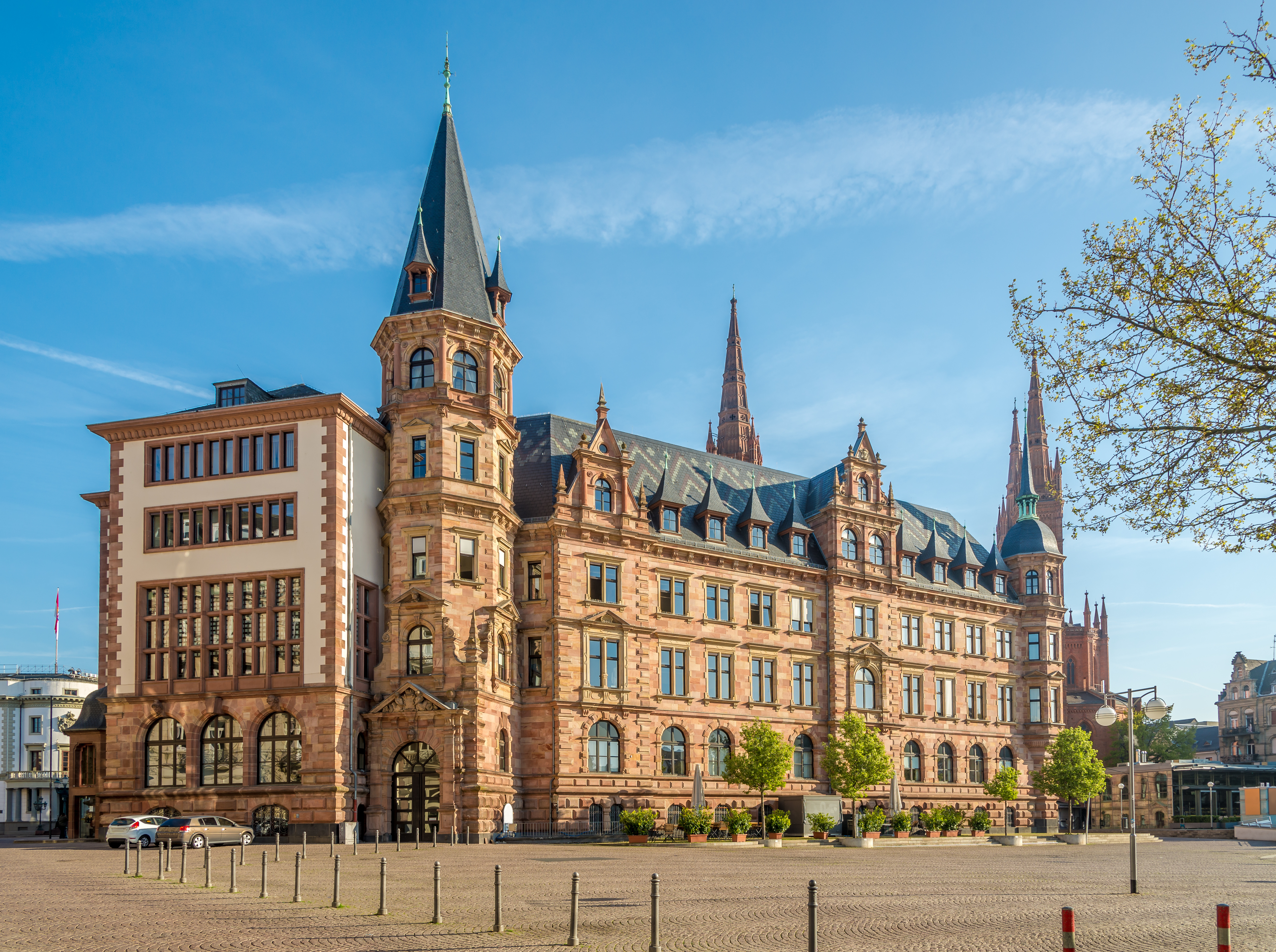 Großes, historisches Wohngebäude mit Türmen und vielen Fenstern, davor Bäume und ein Platz.