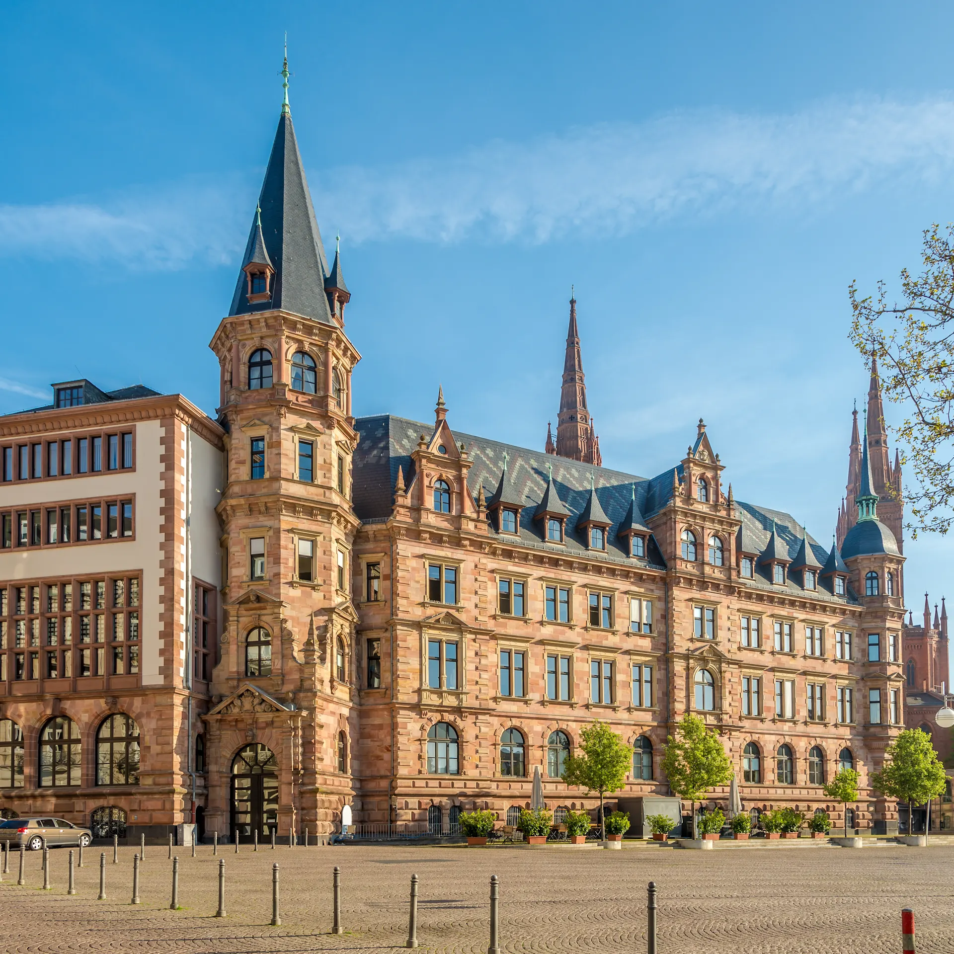 Großes, historisches Wohngebäude mit Türmen und vielen Fenstern, davor Bäume und ein Platz.