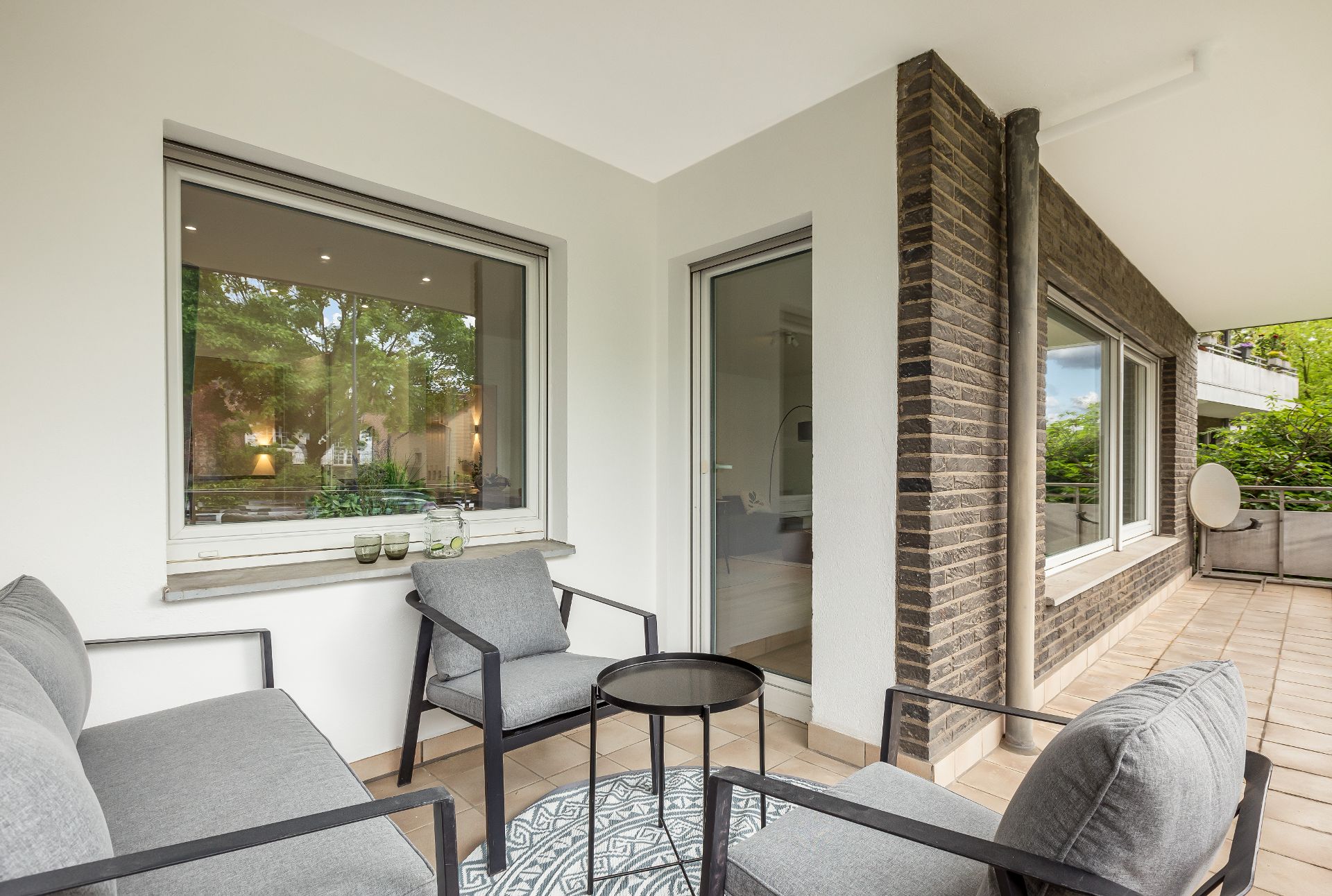 Überdachte Terrasse mit grauen Stühlen, Sofa, kleinem Tisch und Blick ins Grüne.