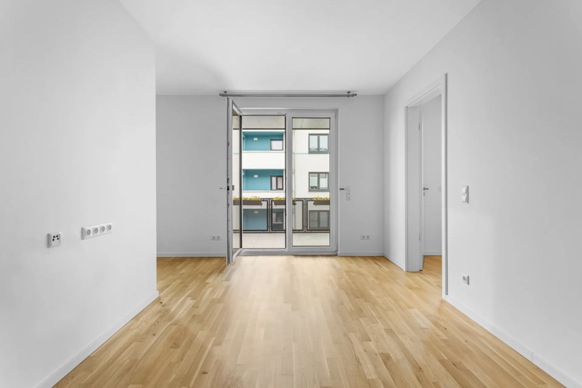 Heller, leerer Raum mit Parkettboden, Fenster und Zugang zum Balkon.