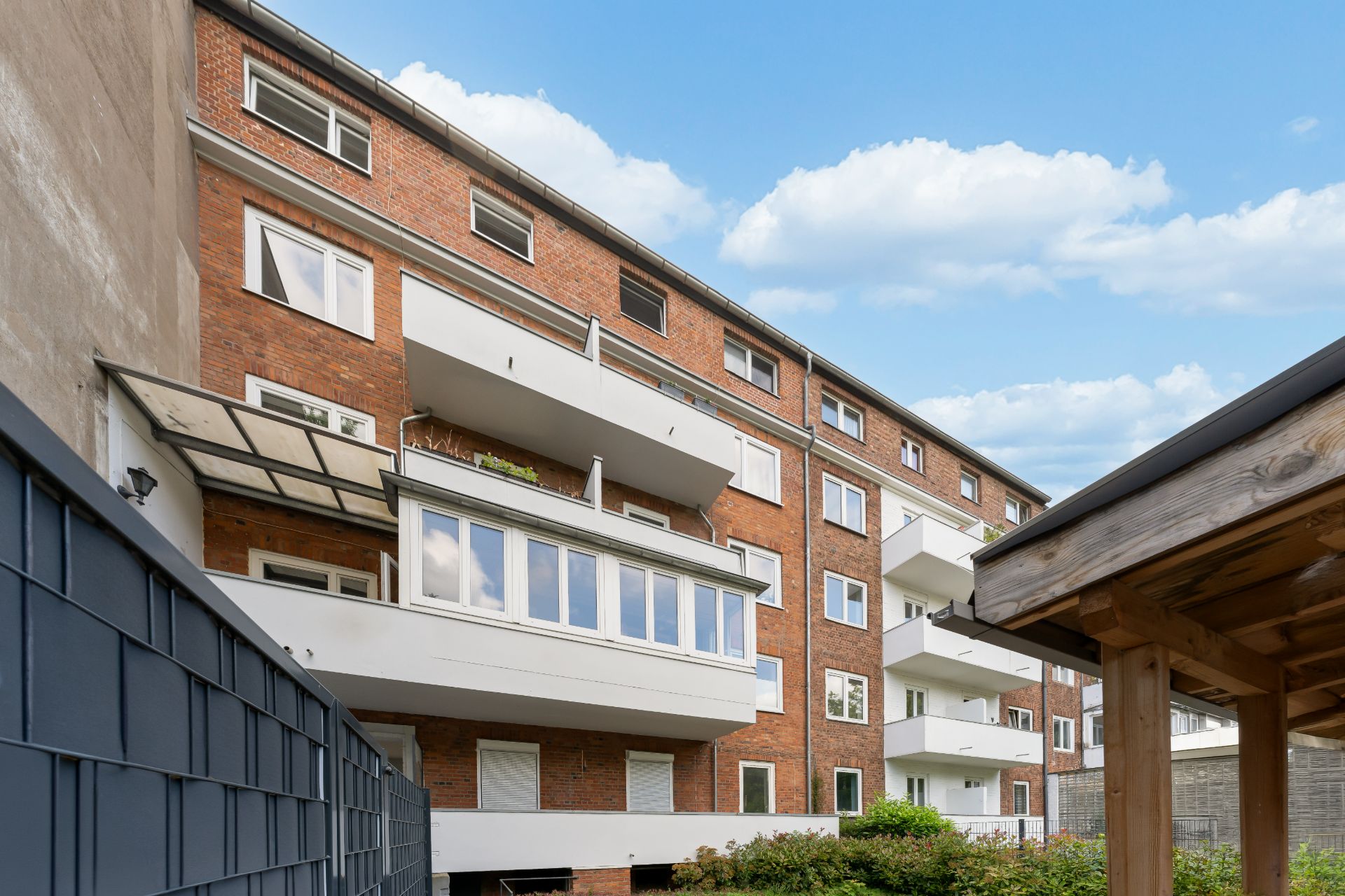 Mehrstöckiges Wohnhaus aus Backstein mit weißen Balkonen und Fenstern, Himmel im Hintergrund.