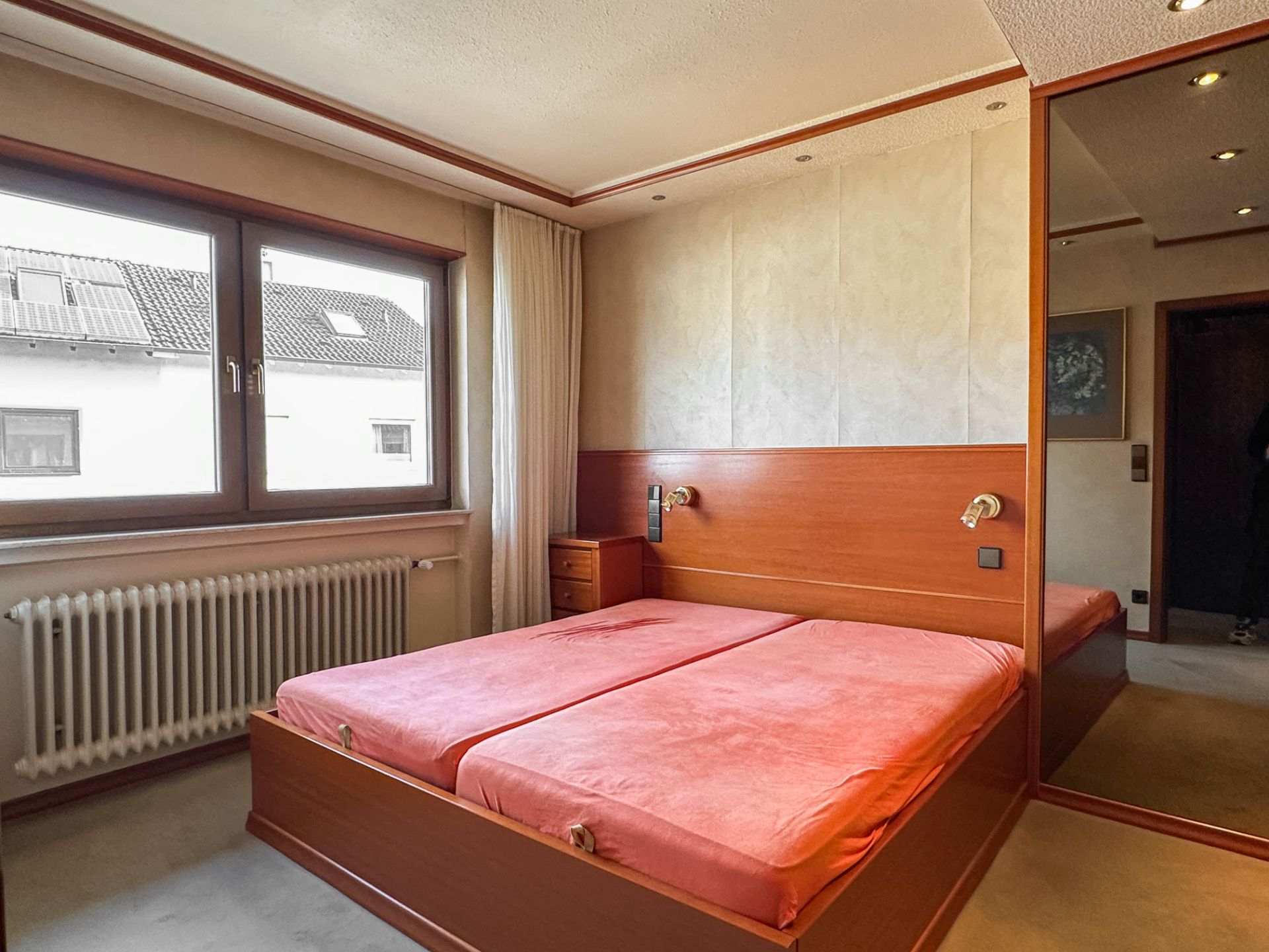 Schlafzimmer mit Doppelbett, Spiegelschrank und großem Fenster mit Blick nach draußen.