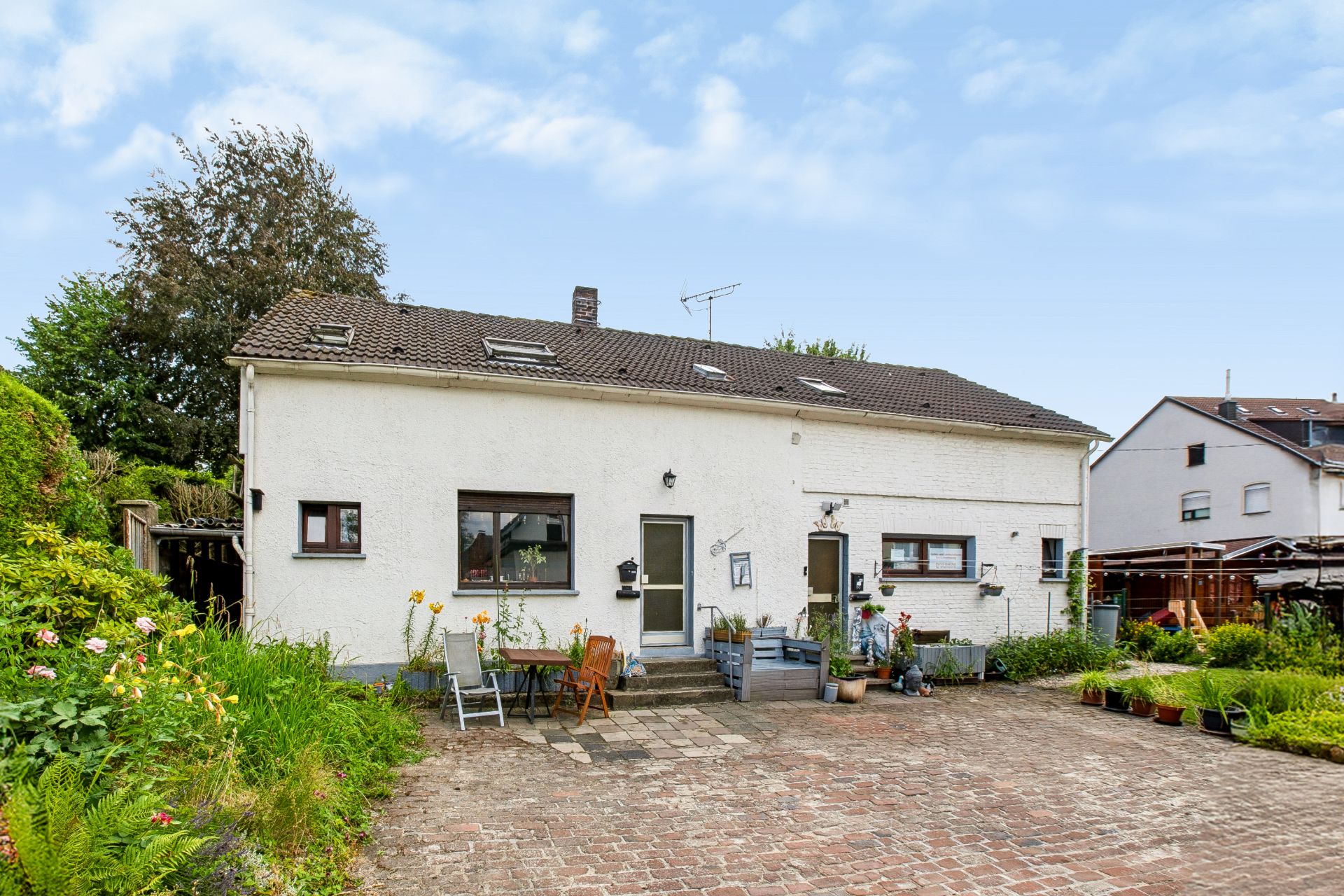 Weiße Doppelhaushälfte mit Garten, Pflasterfläche und Außenmöbeln.