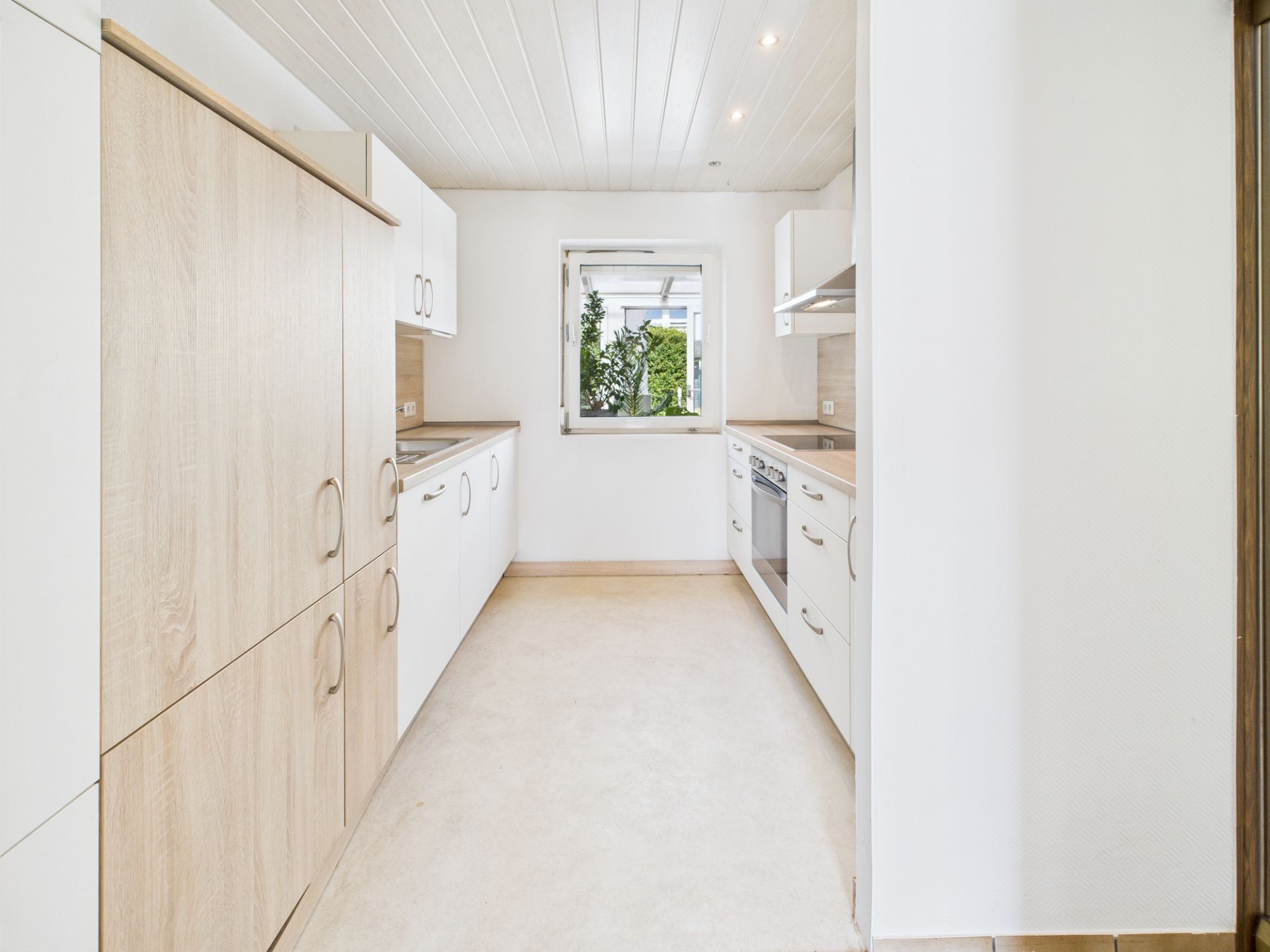 Helle, moderne Küche mit Holzelementen, weißen Schränken und einem Fenster mit Blick nach draußen.