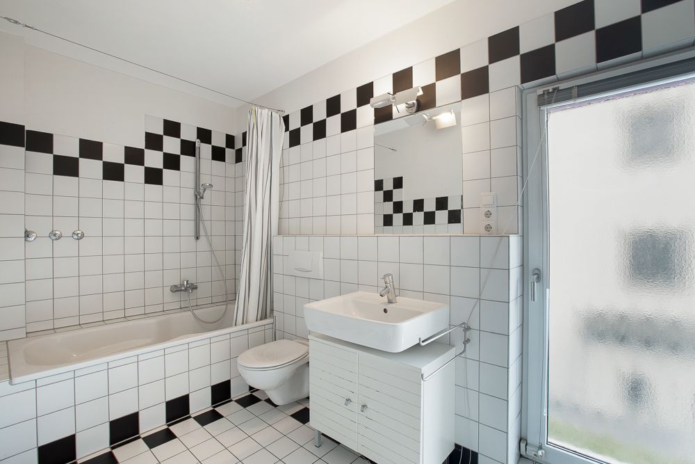 Weiß gefliestes Badezimmer mit Badewanne, Waschbecken, Spiegel und Fenster.