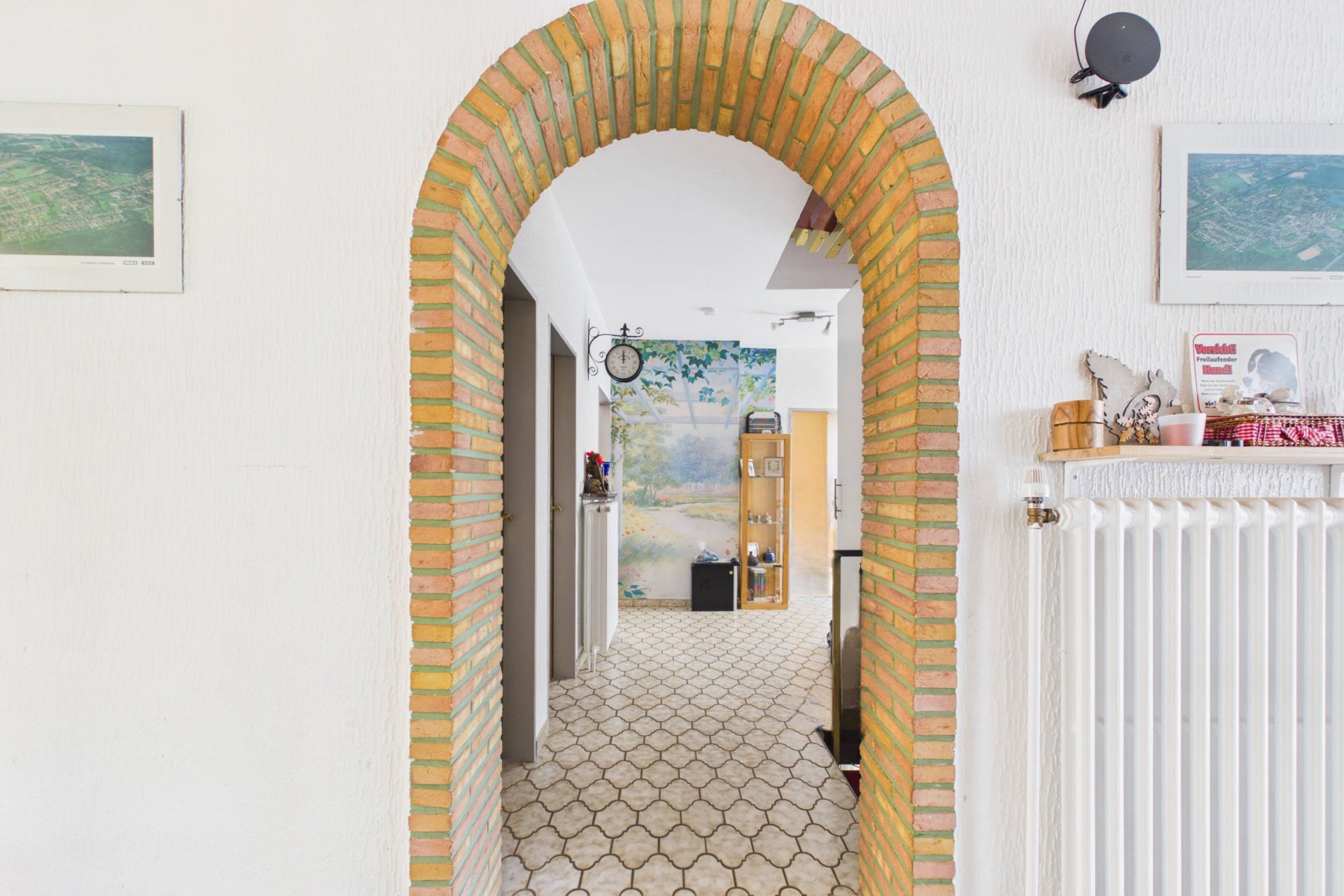 Flur mit gemauertem Torbogen, Fliesenboden und Wandheizkörper in einem Wohnhaus.