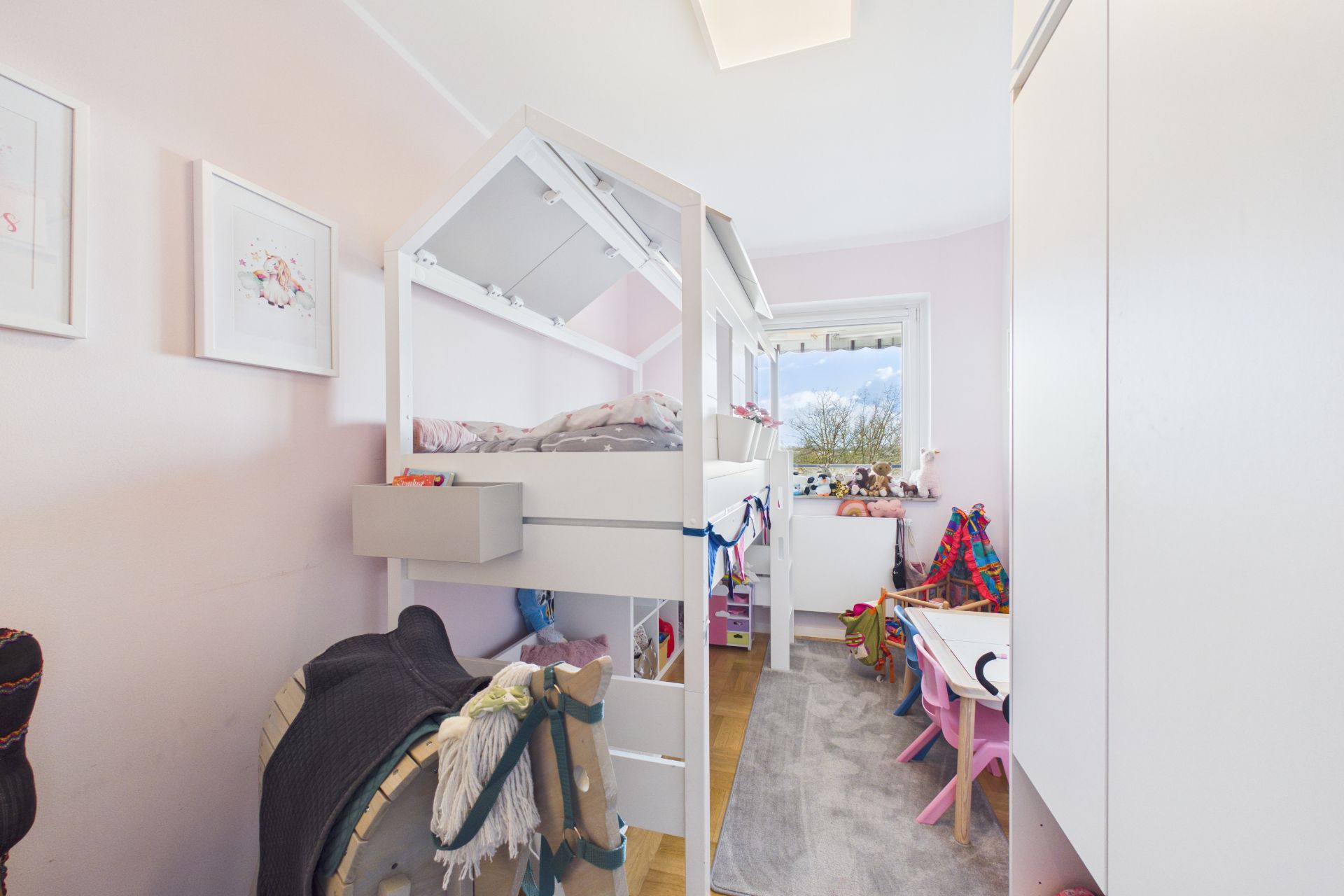 Helles Kinderzimmer mit Hochbett, Schreibtisch und Fenster, dekoriert mit Spielzeug.