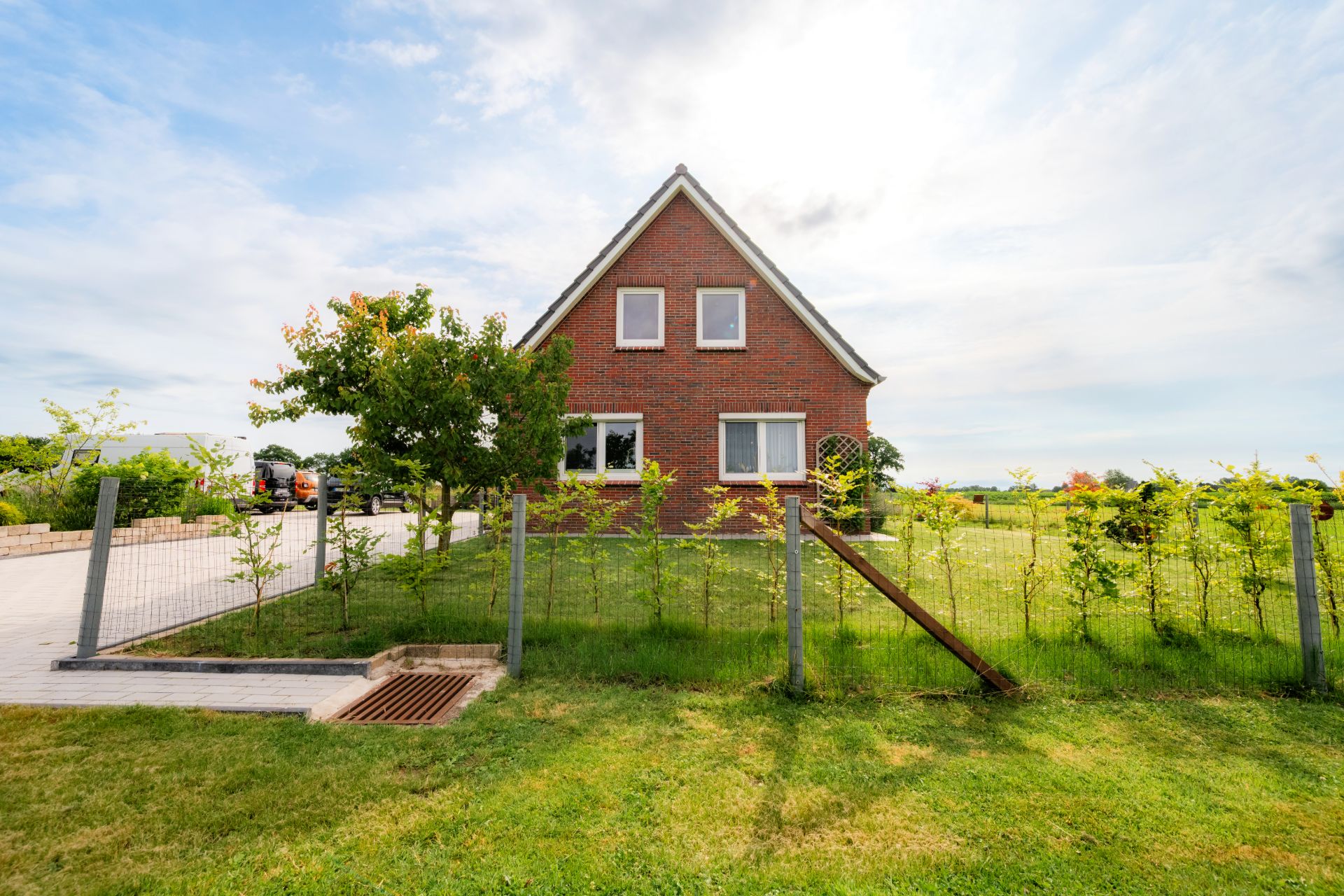Ein rotes Backsteinhaus mit Garten und kleinem Zaun im Vordergrund bei Tageslicht.