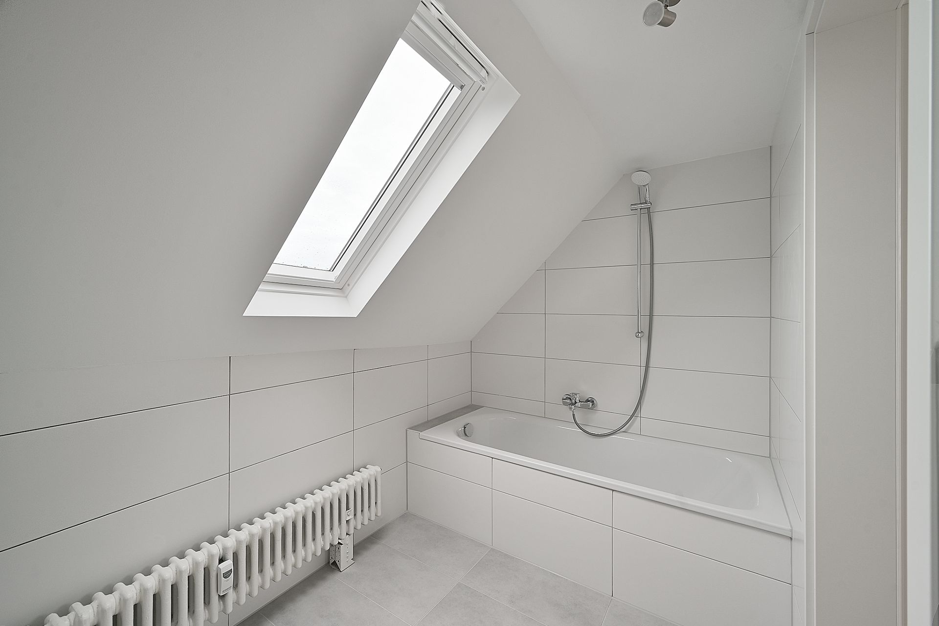 Helles Badezimmer mit Badewanne, Dachfenster und Heizkörper unter einer Schräge.
