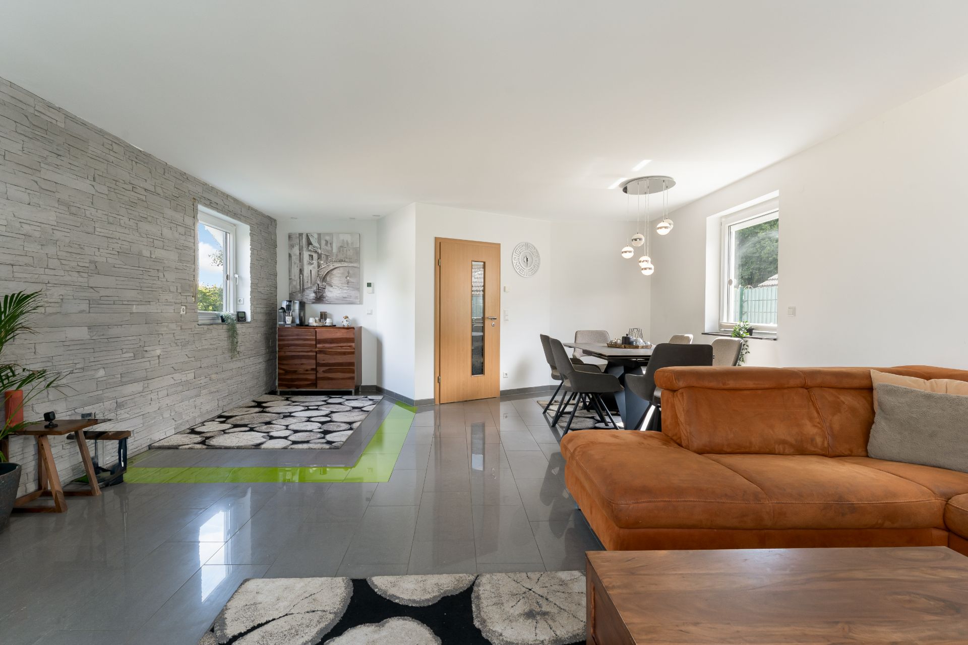 Modernes Wohnzimmer mit braunem Sofa, Esstisch, Steinwand und großen Fenstern.