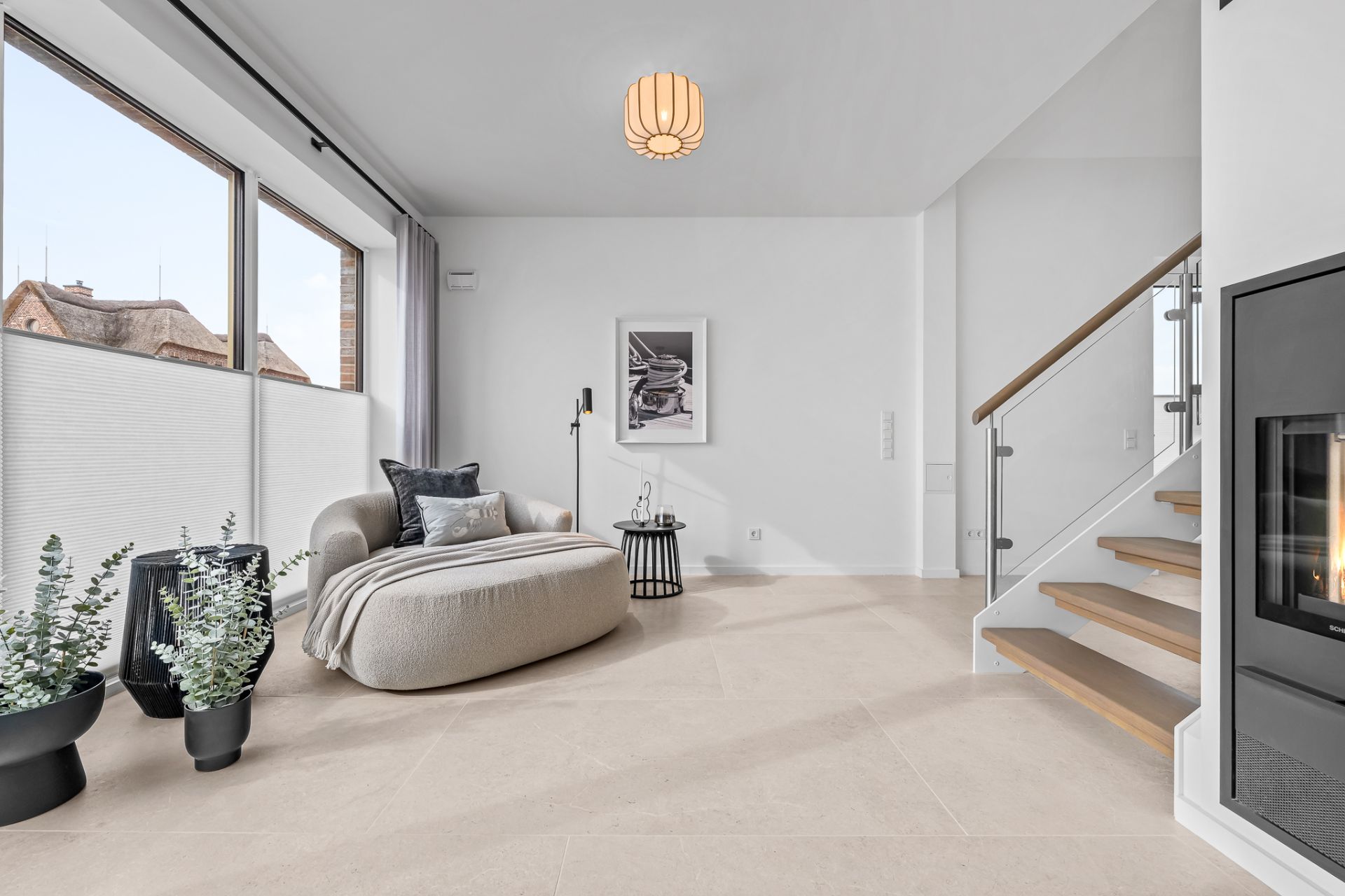 Modernes Wohnzimmer mit großem Fenster, Sessel, Beistelltisch, Pflanzen und Treppe.