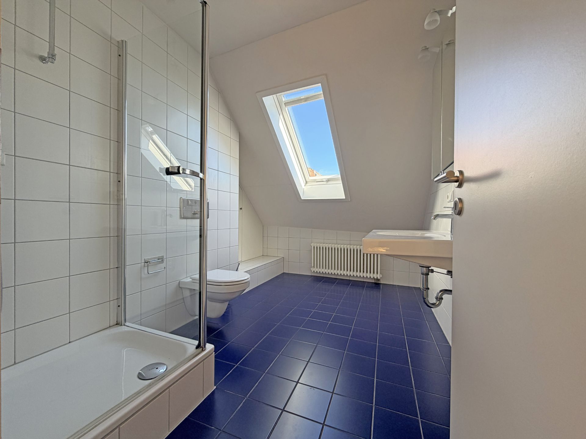 Modernes Bad mit blauen Fliesen, Dusche, WC, Waschbecken und Dachfenster.