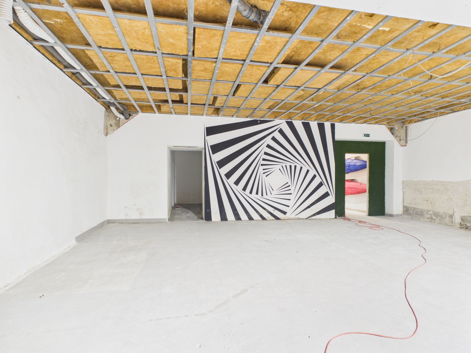 Leerer Raum mit offener Decke und Wandbild mit schwarz-weißem Spiralmuster.