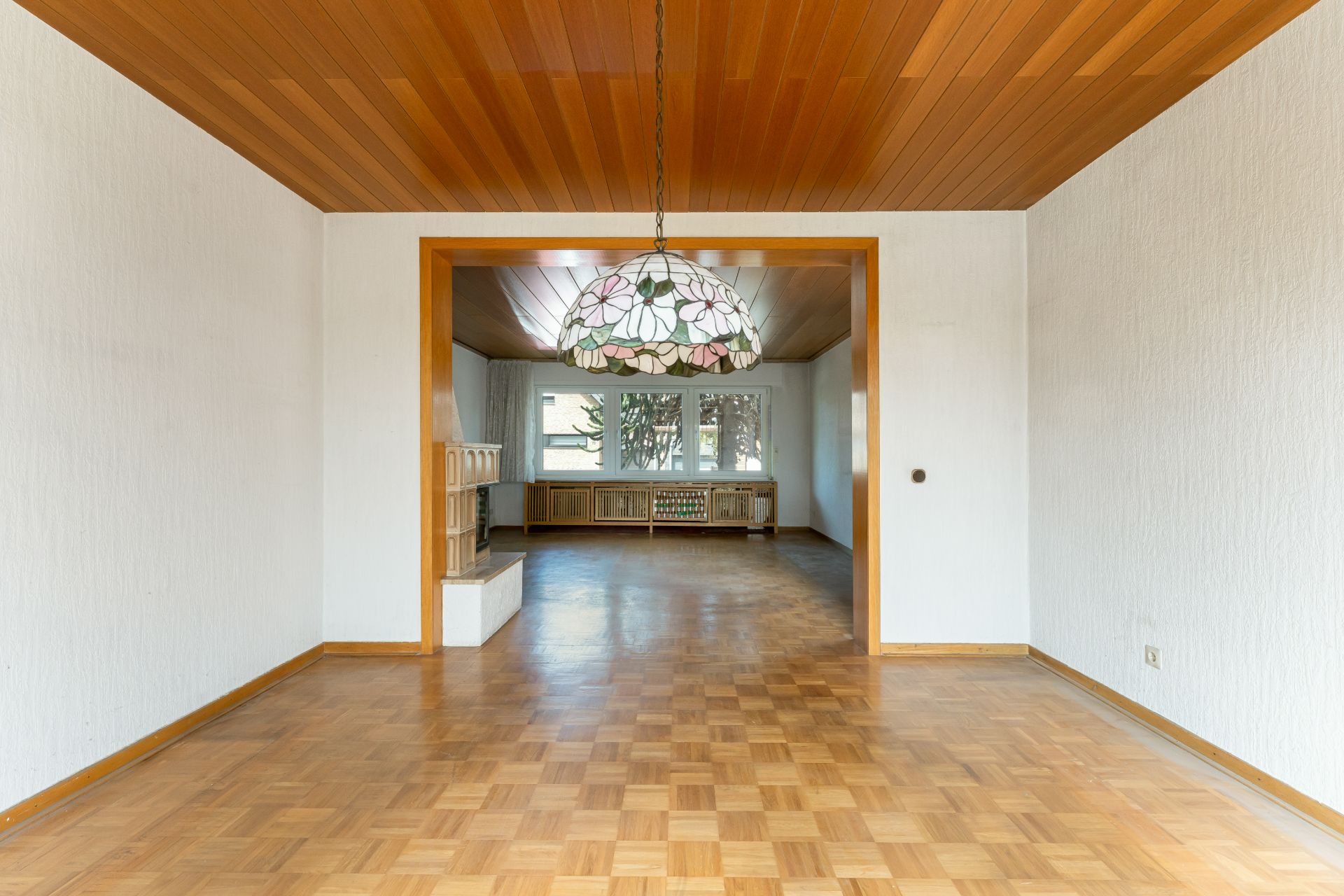 Zwei leere verbundene Räume mit Parkettboden und Hängelampe, großes Fenster im Hintergrund.