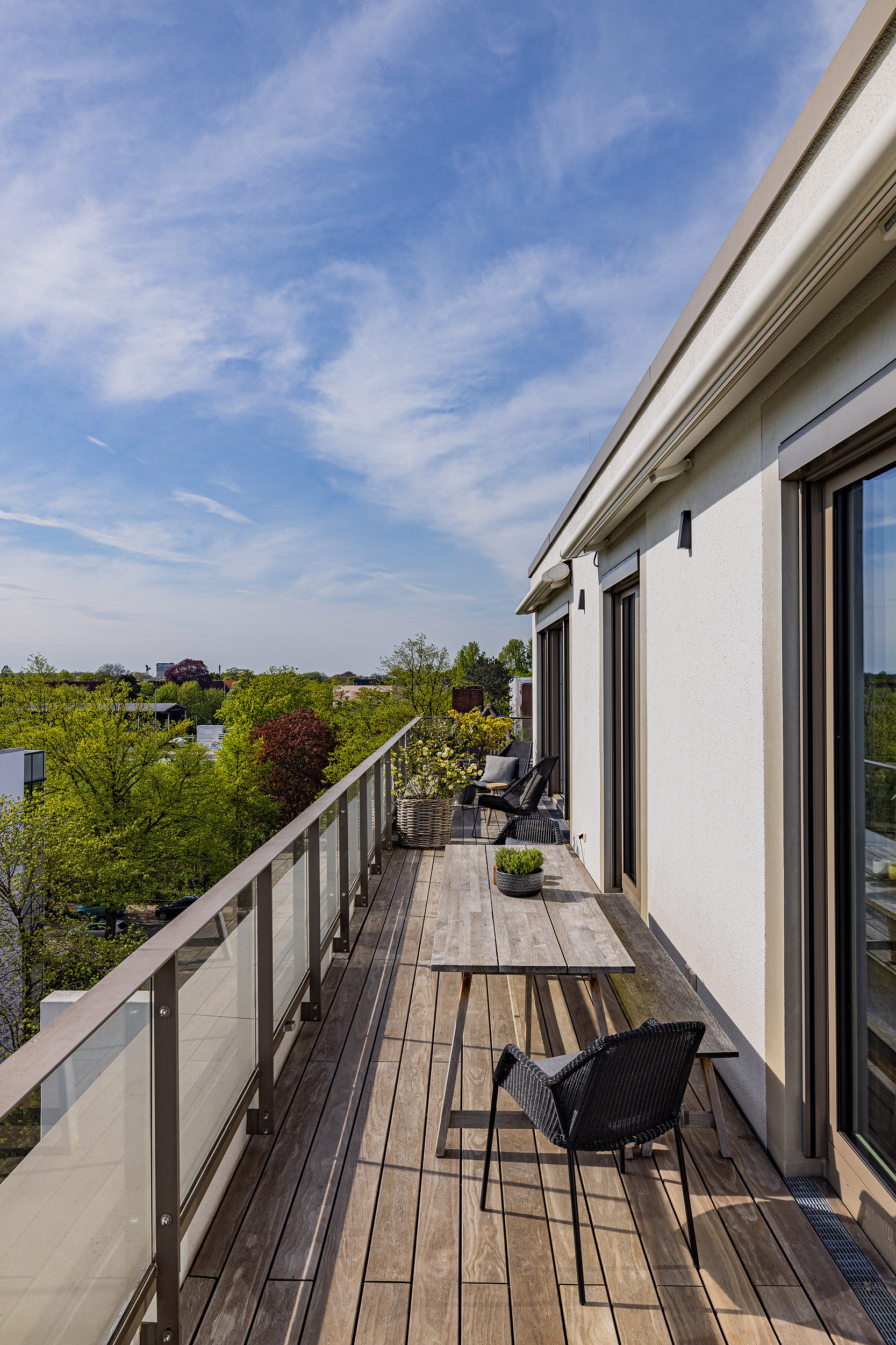 Großer Balkon mit Holzboden, Tisch, Stühlen und Pflanzen, Ausblick ins Grüne.