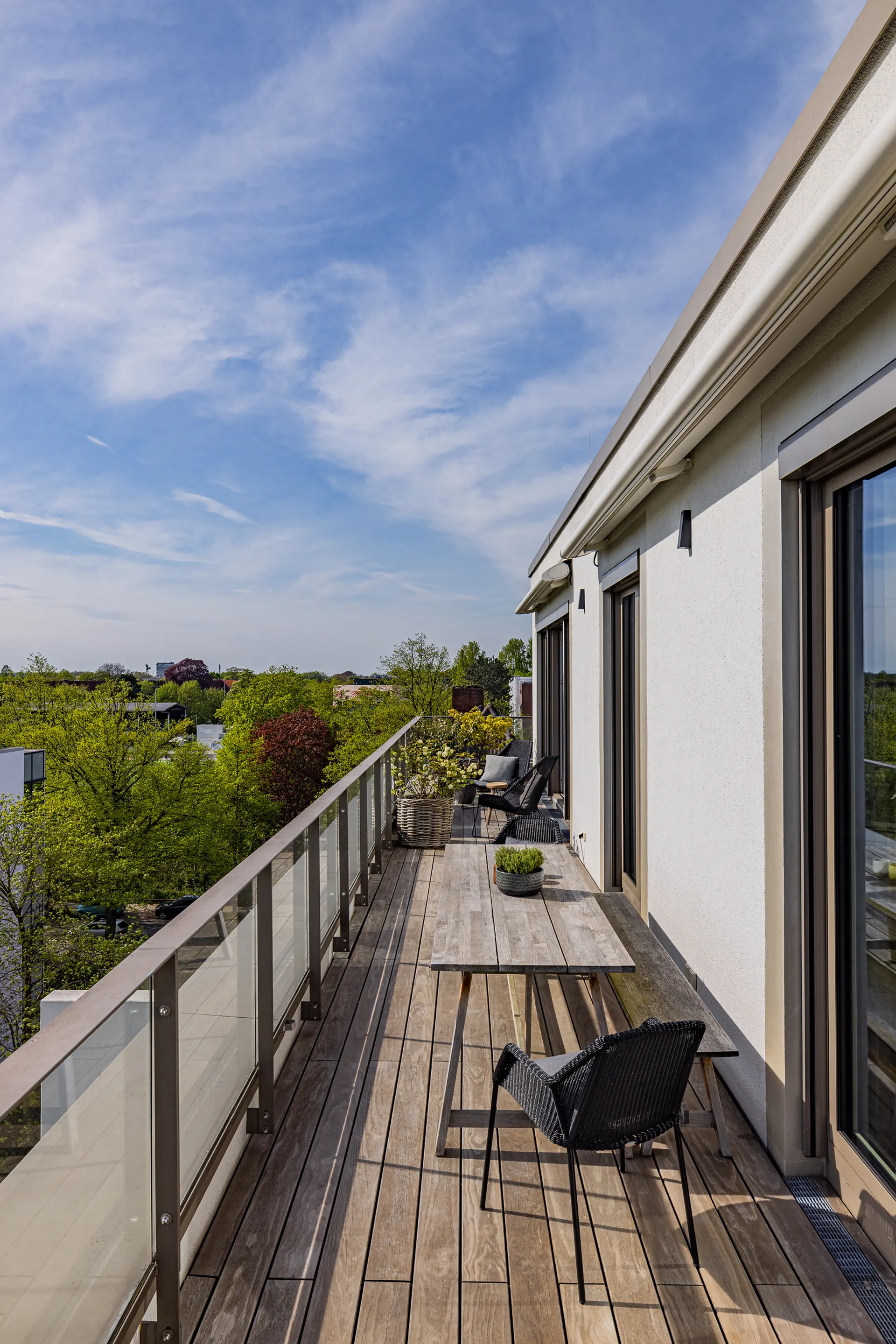 Großer Balkon mit Holzboden, Tisch, Stühlen und Pflanzen, Ausblick ins Grüne.