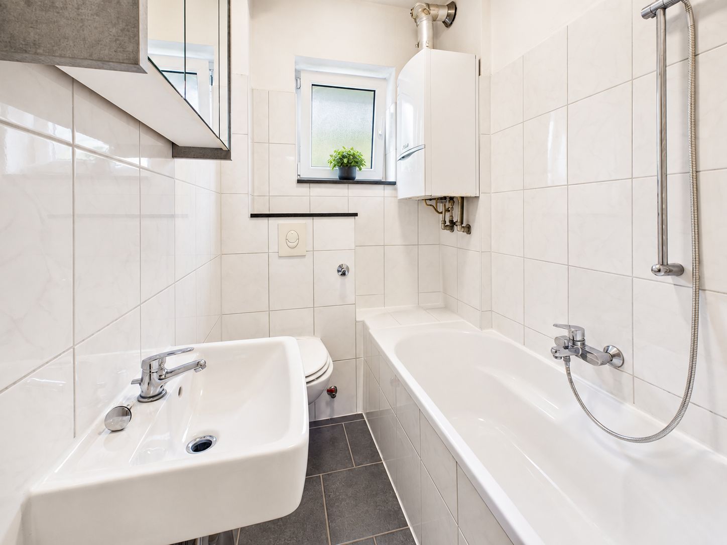 Helles Badezimmer mit Badewanne, Waschbecken, WC und kleinem Fenster mit Pflanze.