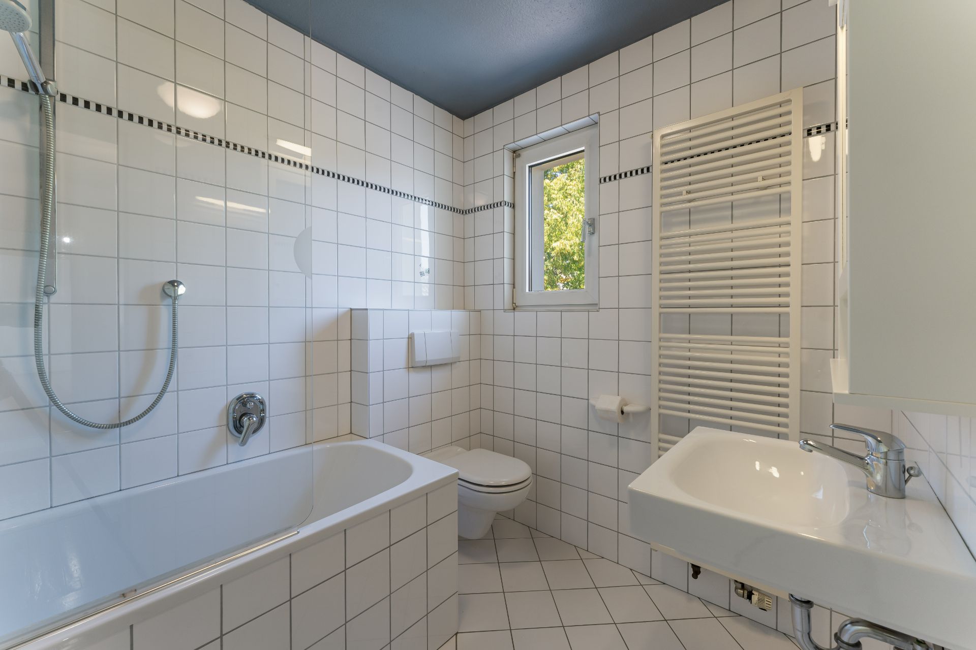 Helles Badezimmer mit Badewanne, WC, Waschbecken, Fenster und Handtuchheizkörper.