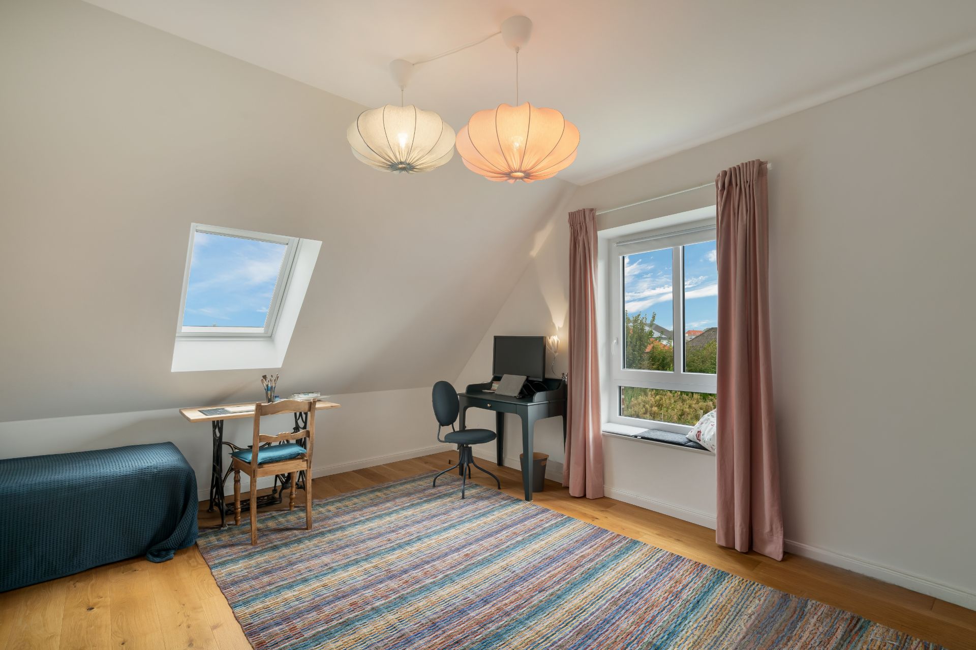 Helles Zimmer mit Schreibtisch, Stuhl, Teppich und Fenster mit rosa Vorhang.