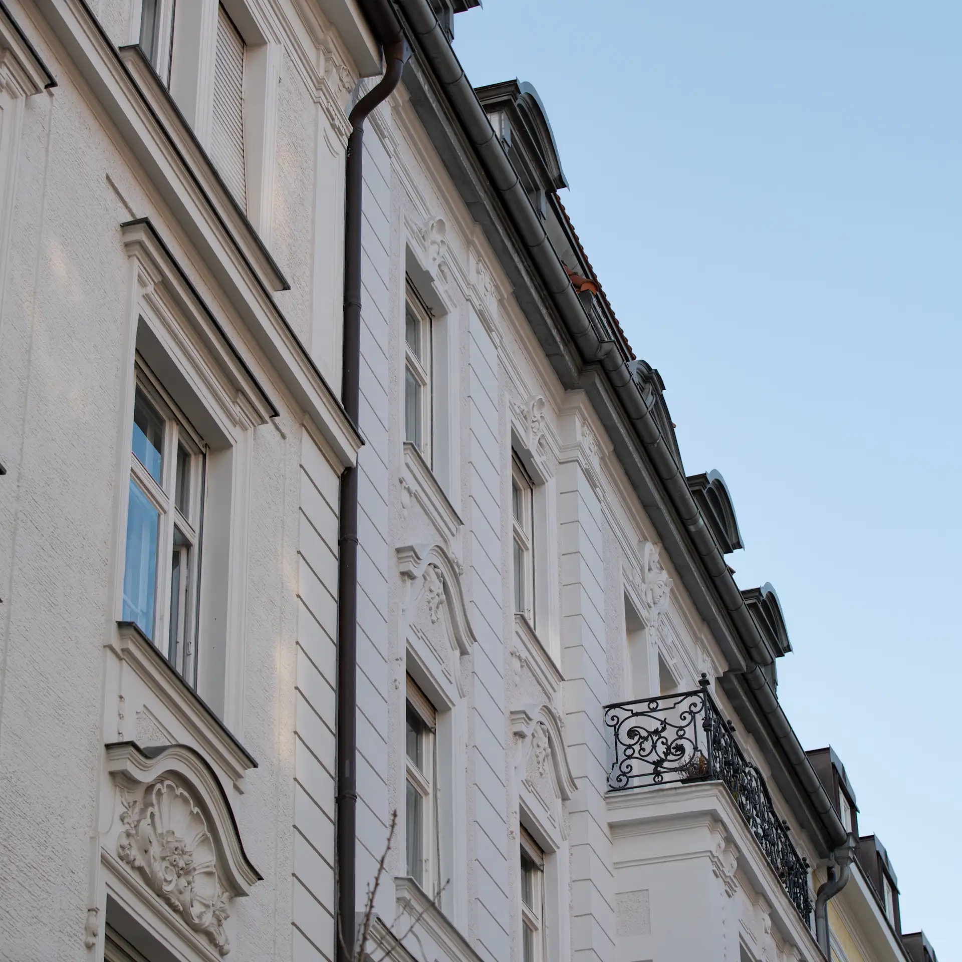 Fassade eines weißen Wohnhauses mit verzierten Fenstern und schmiedeeisernem Balkon.