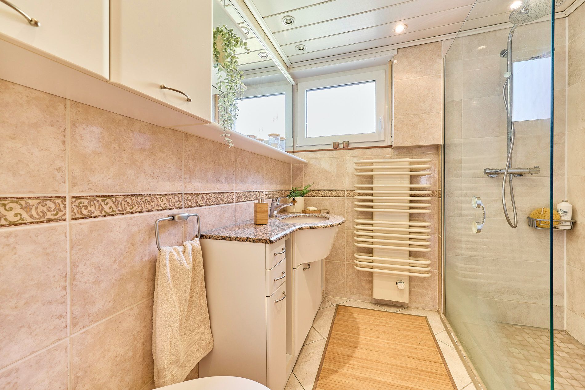 Helles Badezimmer mit Waschbecken, Handtuch, Heizung und ebenerdiger Dusche.