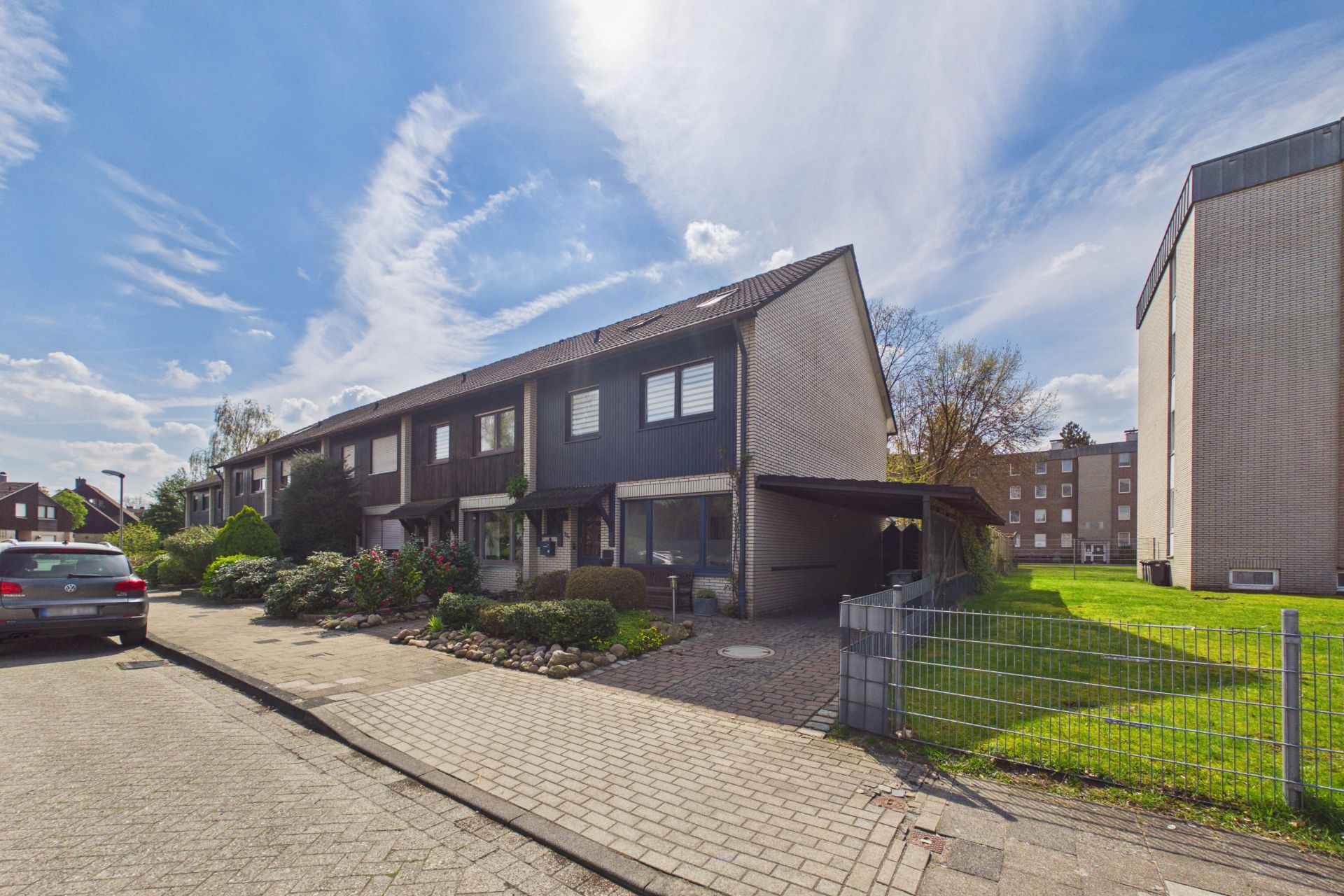 Reihenhaus mit Vorgarten, Carport und angrenzender Grünfläche an einer Wohnstraße.