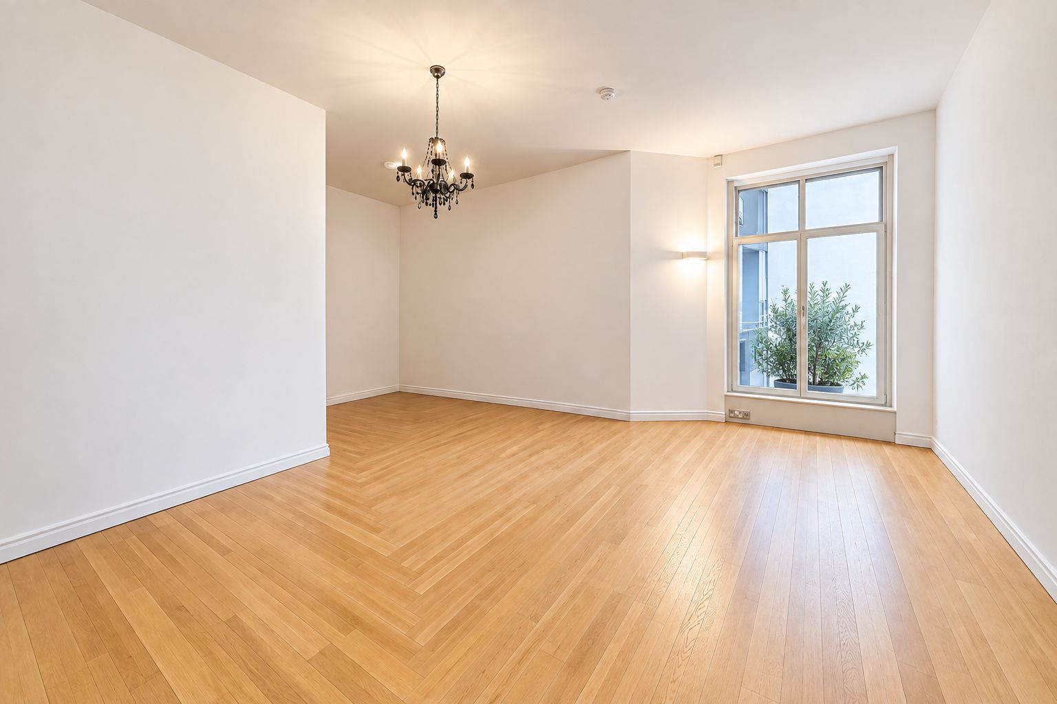 Heller leerer Raum mit Holzfußboden, großem Fenster und Kronleuchter.