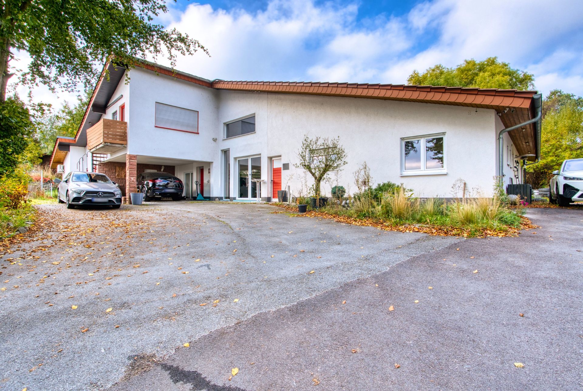 Modernes Wohnhaus mit flachem Dach, Auffahrt, zwei geparkten Autos und bepflanztem Vorgarten.